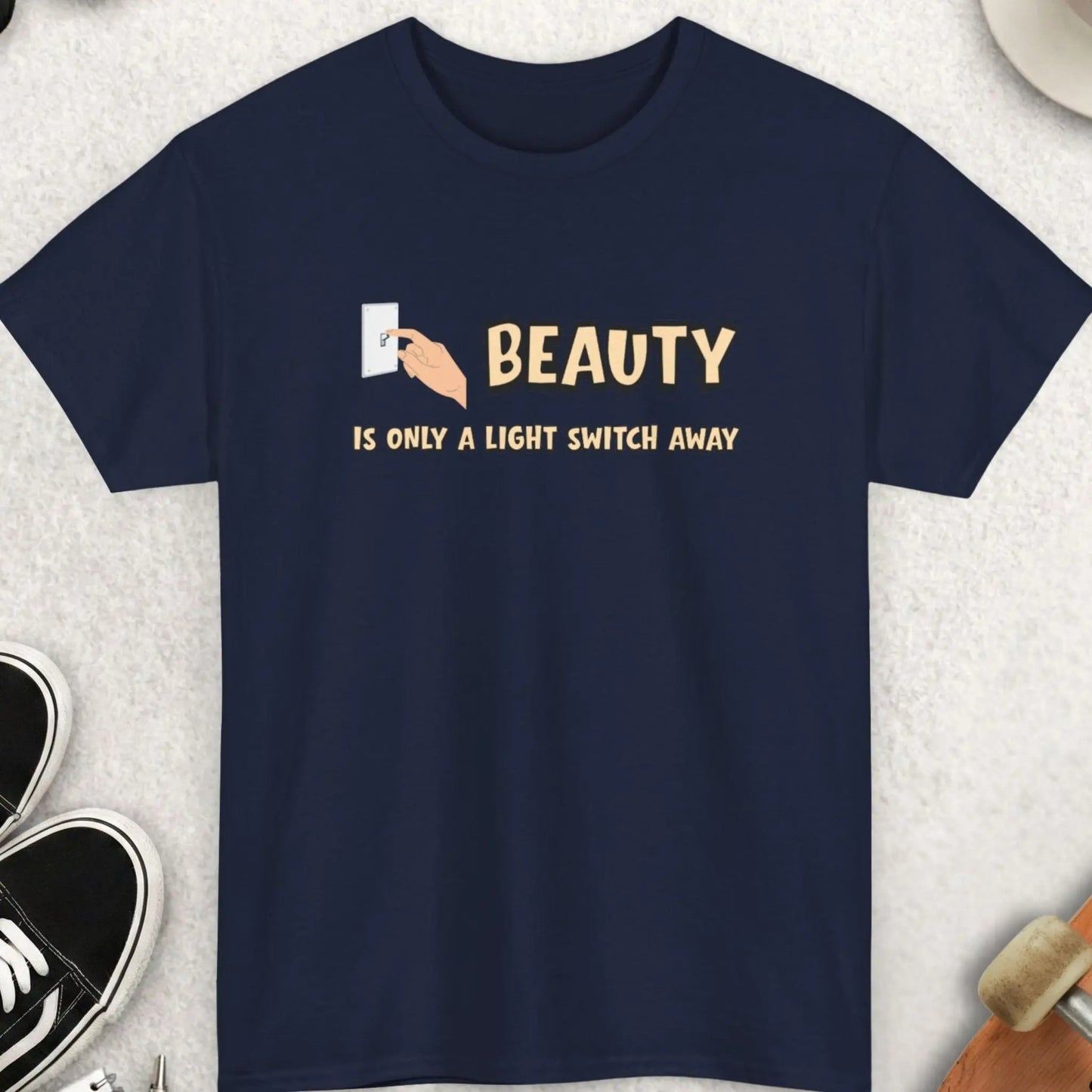 Navy blue t-shirt with 'Beauty is only a light switch away' text on a textured surface with accessories.