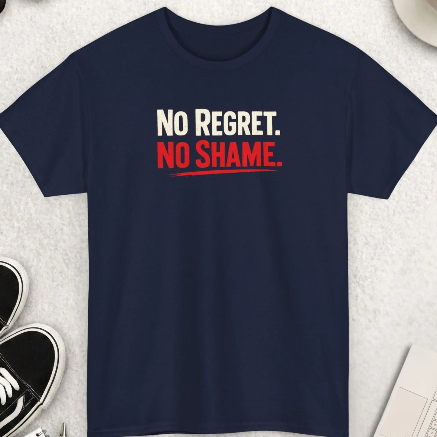 Navy blue t-shirt with 'No Regret. No Shame.' text on a light gray surface with shoes, coffee, and accessories.