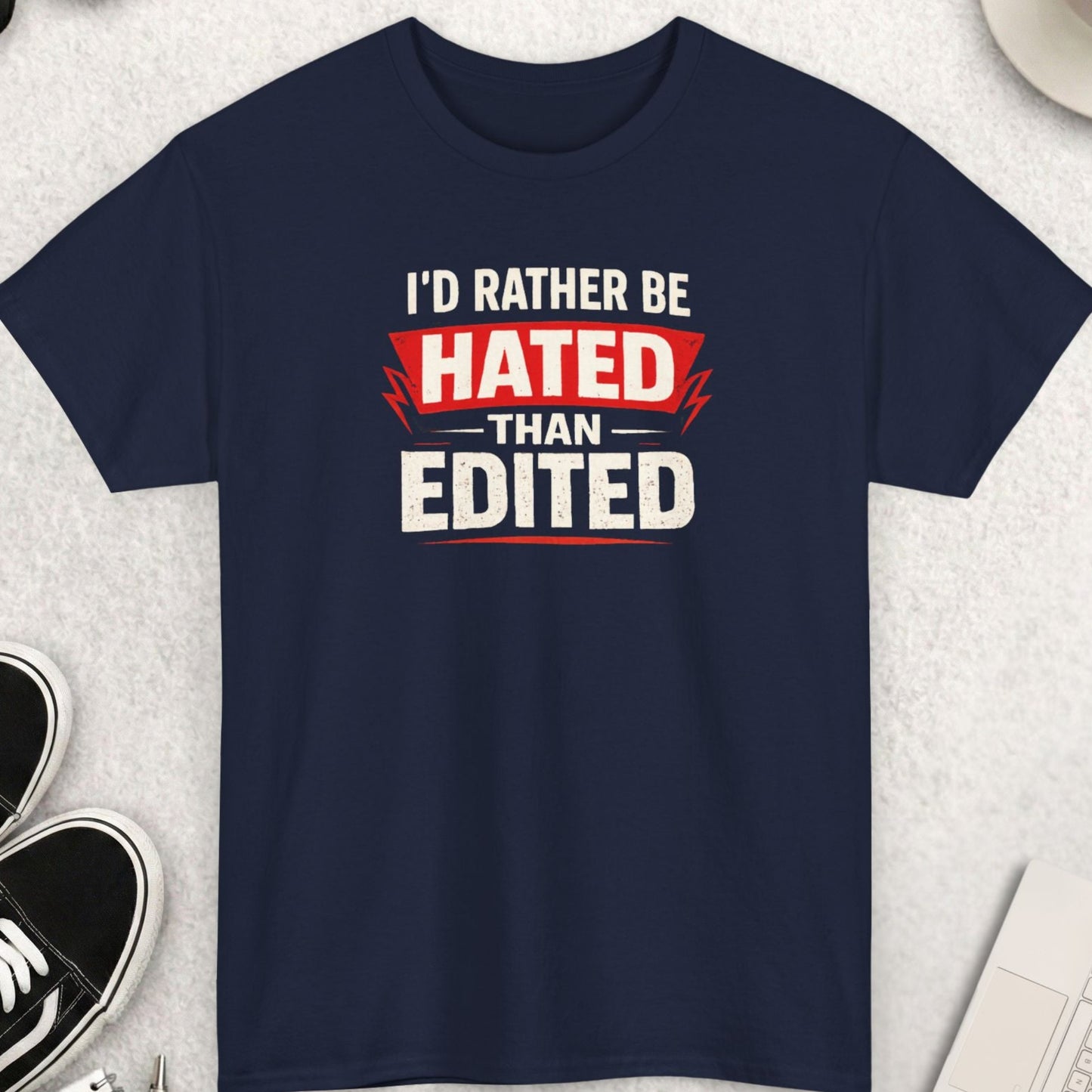 Navy blue t-shirt with text 'I'd Rather Be Hated Than Edited' on a light gray surface with shoes, coffee, and accessories.