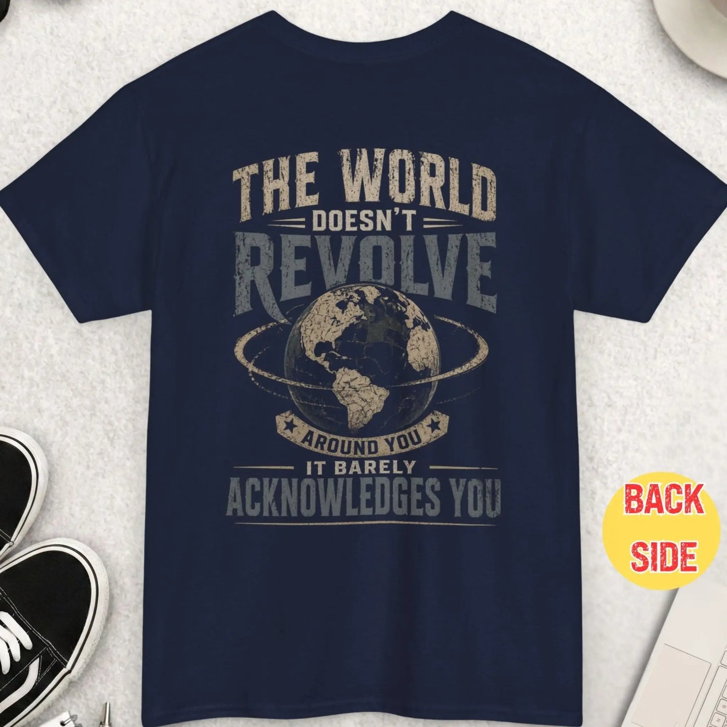 Navy blue t-shirt with distressed typography stating “The World Doesn’t Revolve Around You It Barely Acknowledges You” and a central globe illustration in a vintage worn style.