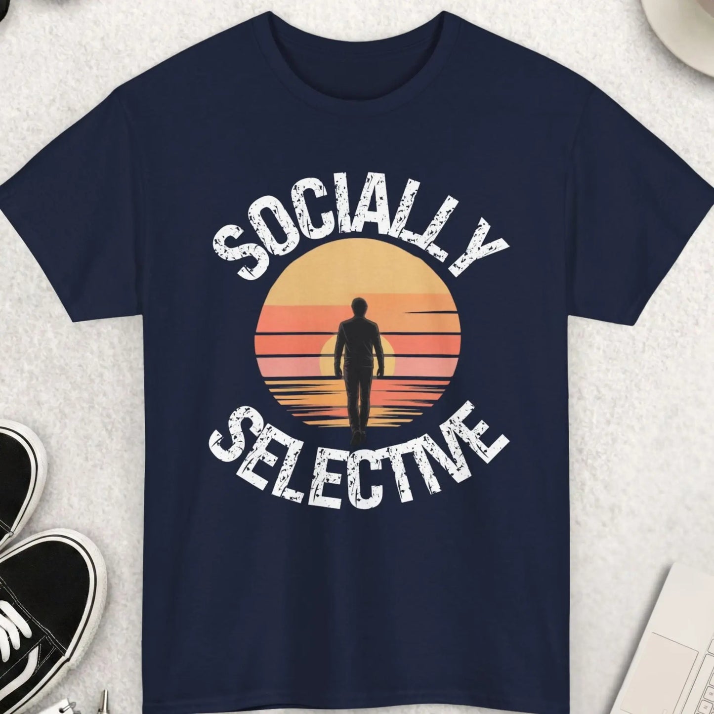 Navy blue t-shirt with 'Socially Selective' design on a light gray surface with shoes, sunglasses, and coffee.