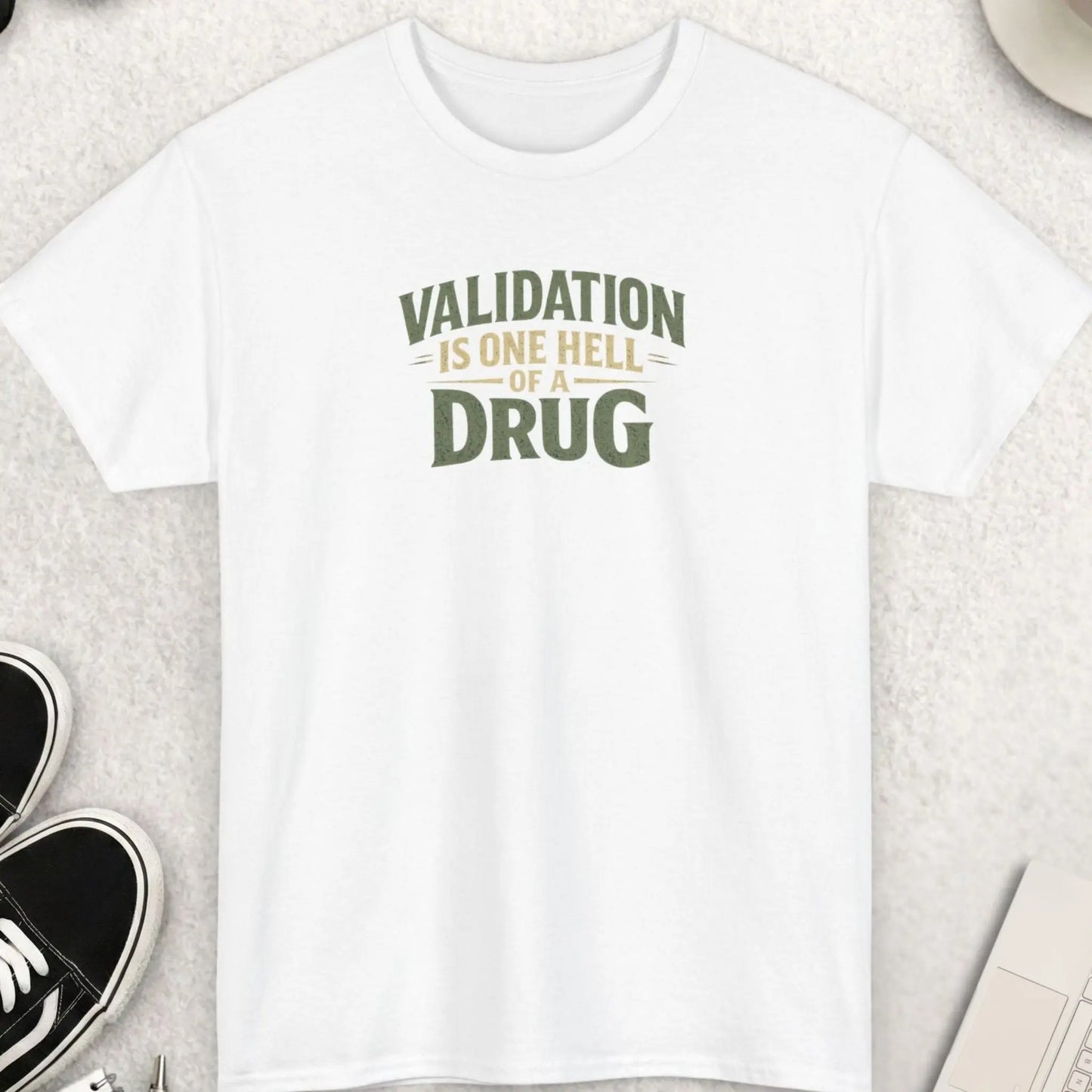 White t-shirt with distressed typography displaying the phrase āValidation Is One Hell Of A Drugā in vintage-inspired green and beige lettering.