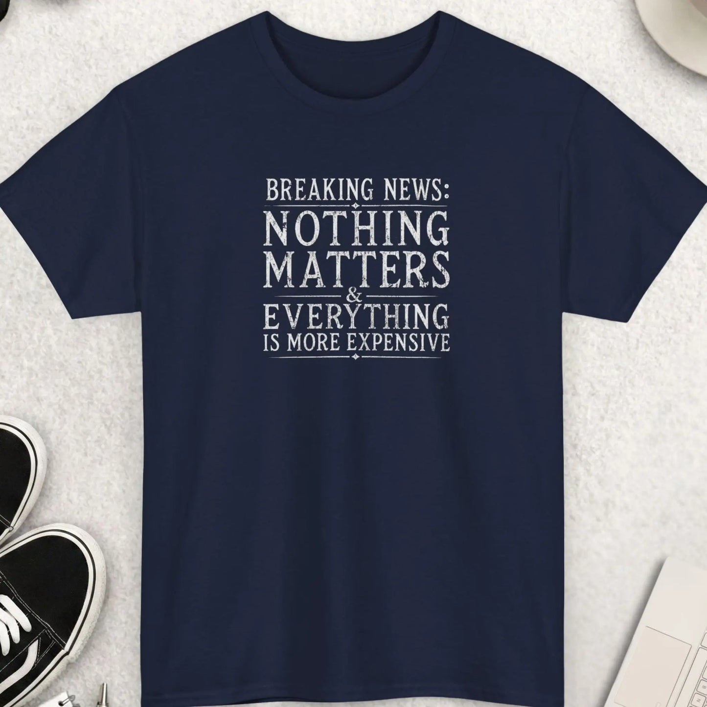 Breaking News: Nothing Matters & Everything Is More Expensive" vintage distressed newspaper-style graphic t-shirt on a navy blue background. Crisp white serif typography with ornate diamond accents and rule lines in a weathered vintage editorial style. Sarcastic inflation humor dark comedy statement graphic tee.