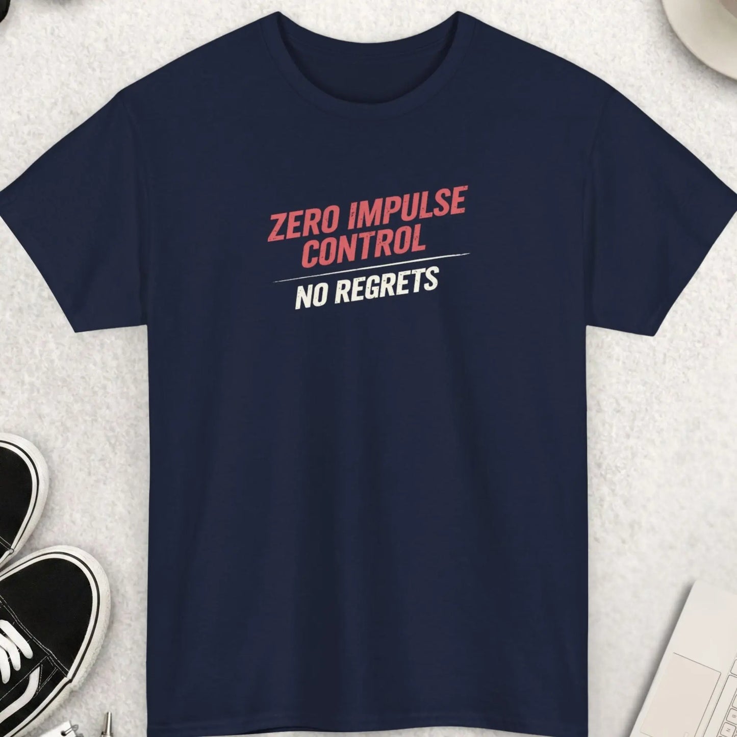 Navy blue t-shirt with 'Zero Impulse Control No Regrets' text on a light gray surface with shoes, coffee, and accessories.