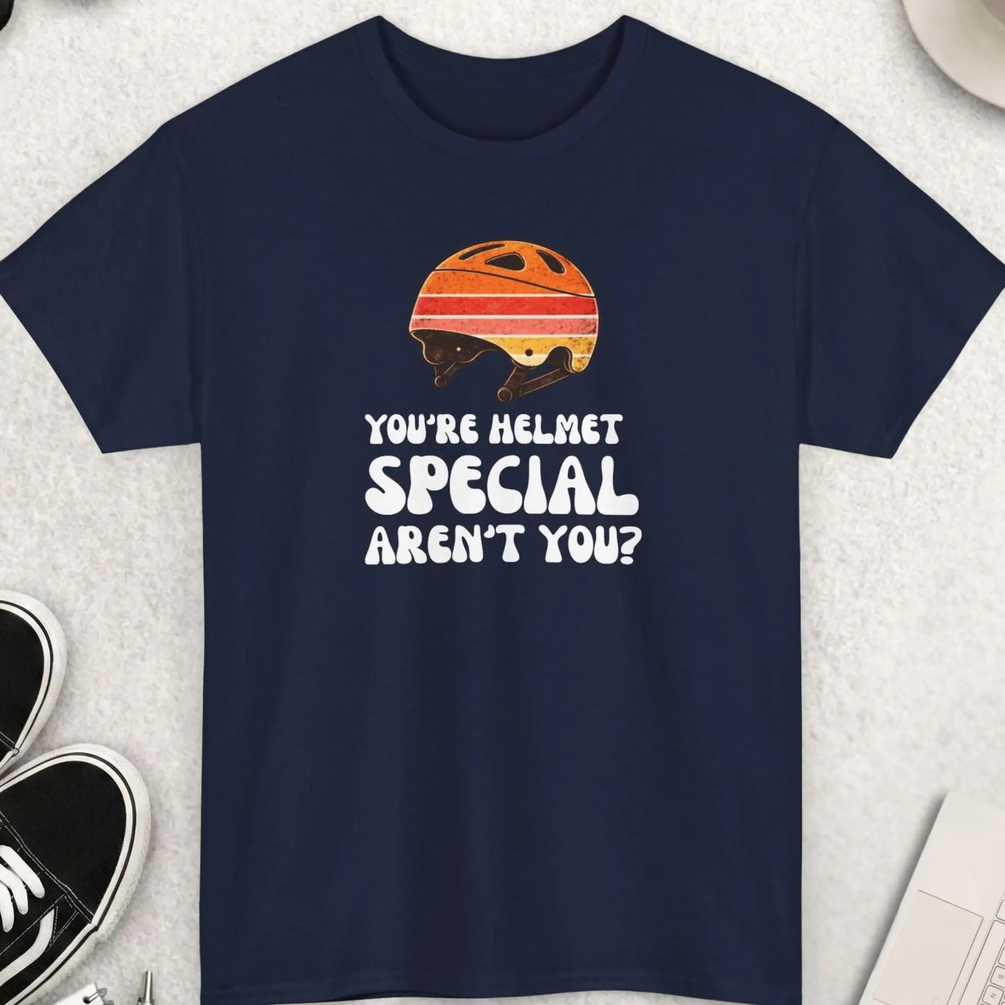 Navy blue t-shirt with a helmet graphic and text on a light gray surface with accessories.