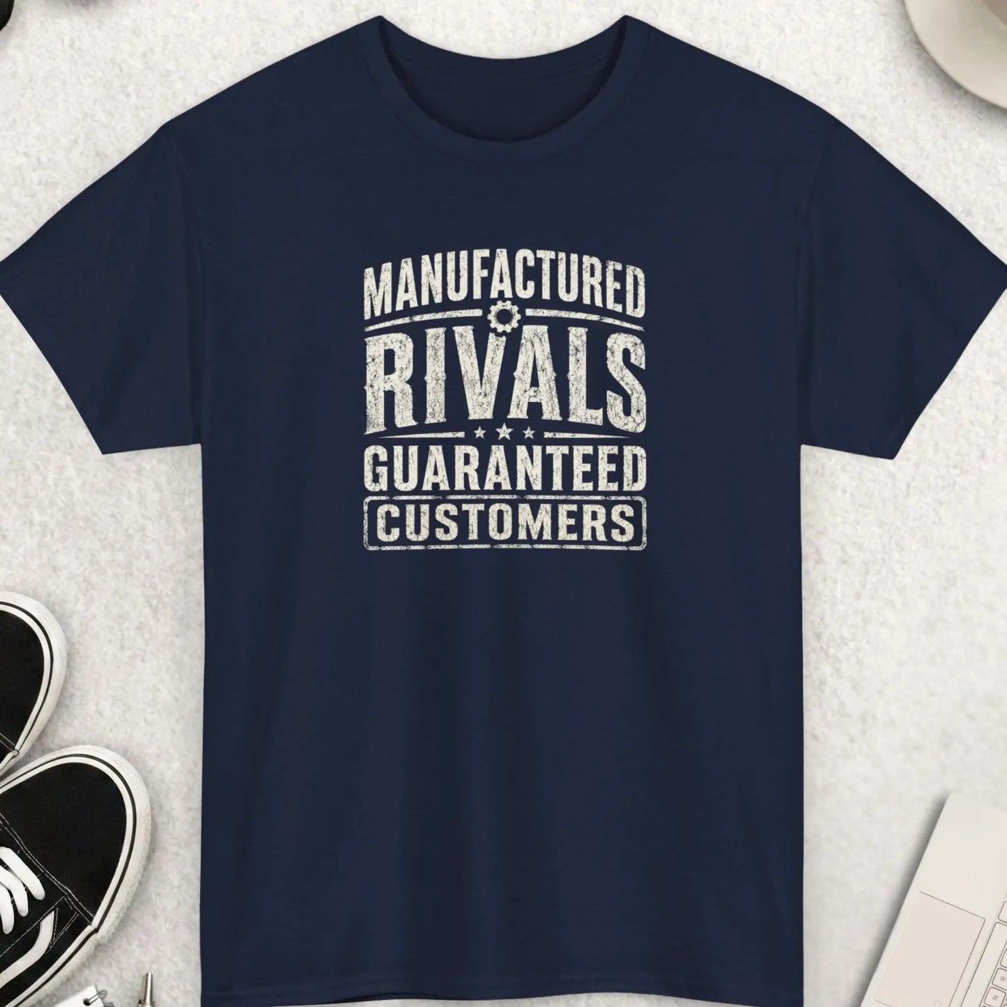 Manufactured Rivals Guaranteed Customers vintage distressed graphic t-shirt featuring aged cream typography on a navy blue shirt with rugged worn print texture, retro styling, and thought-provoking slogan.