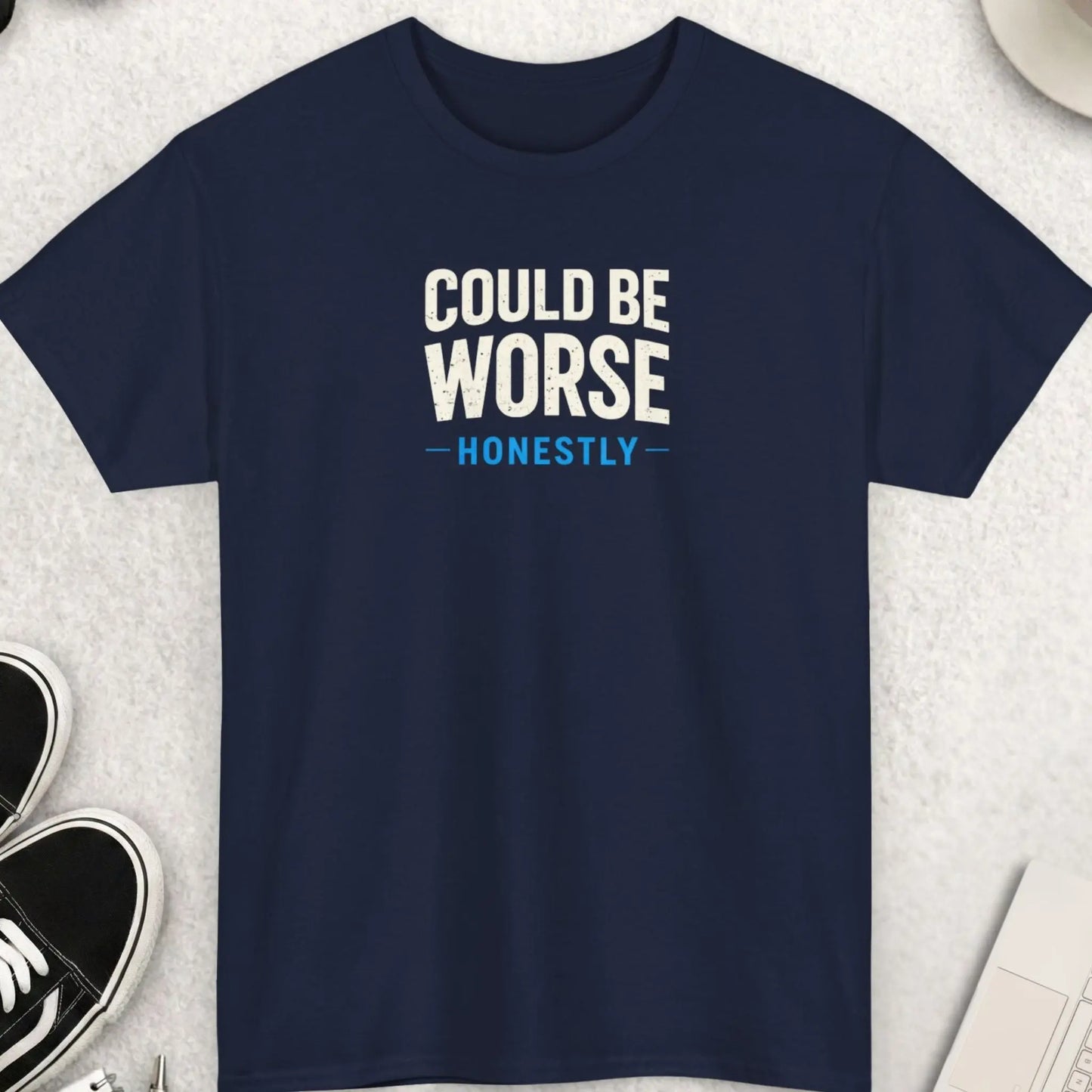 Navy blue t-shirt with 'Could Be Worse Honestly' text on a light gray surface with accessories.