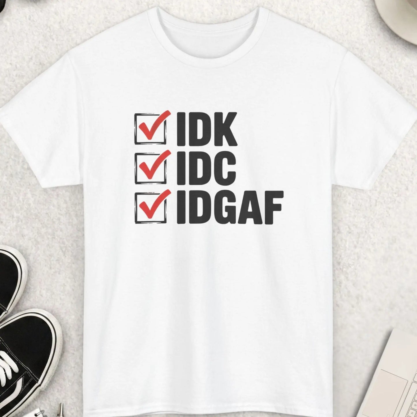 White t-shirt with text 'IDK IDCIDGAF' on a light gray surface with shoes, coffee, and sunglasses.