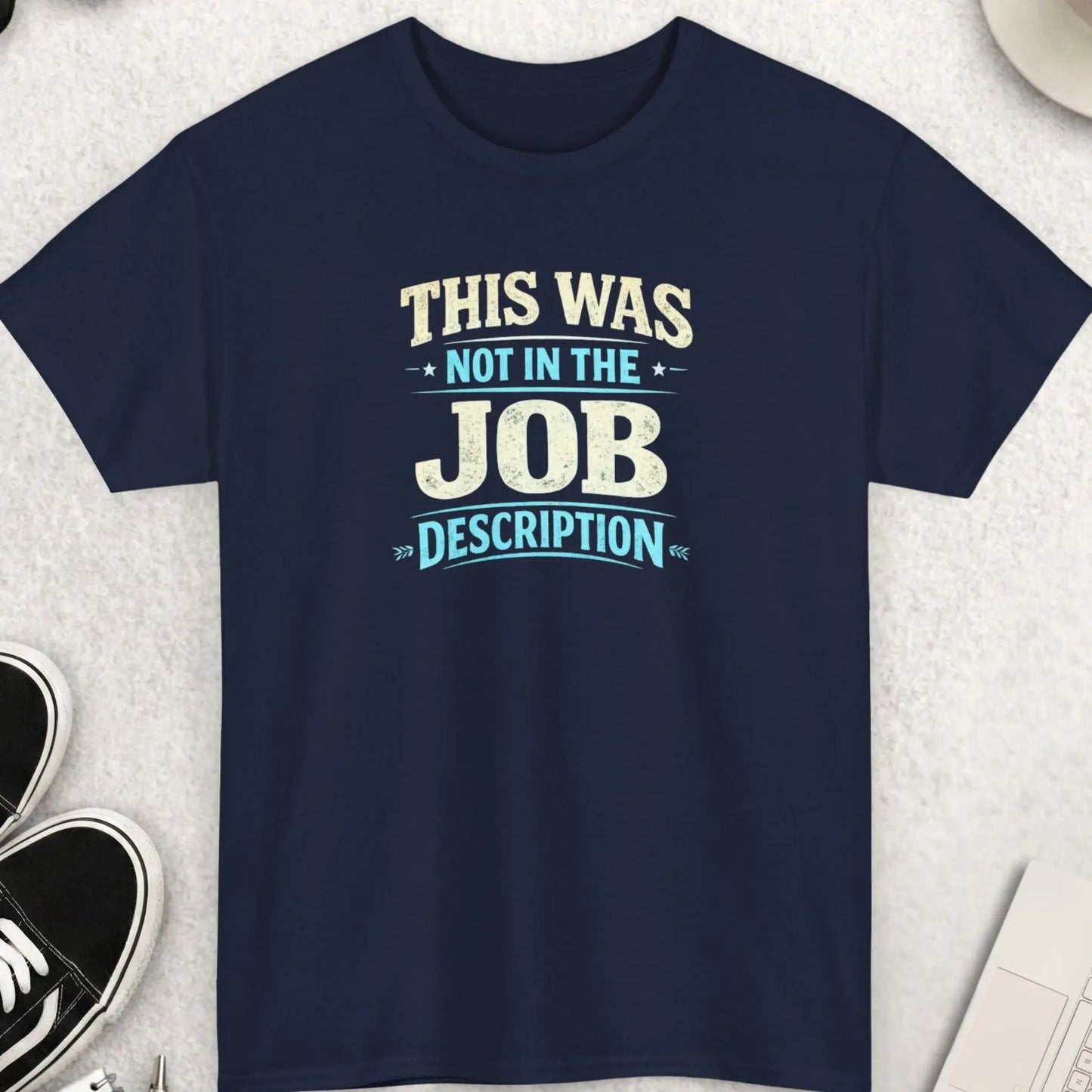 Navy blue t-shirt with humorous text on a light gray surface with accessories.