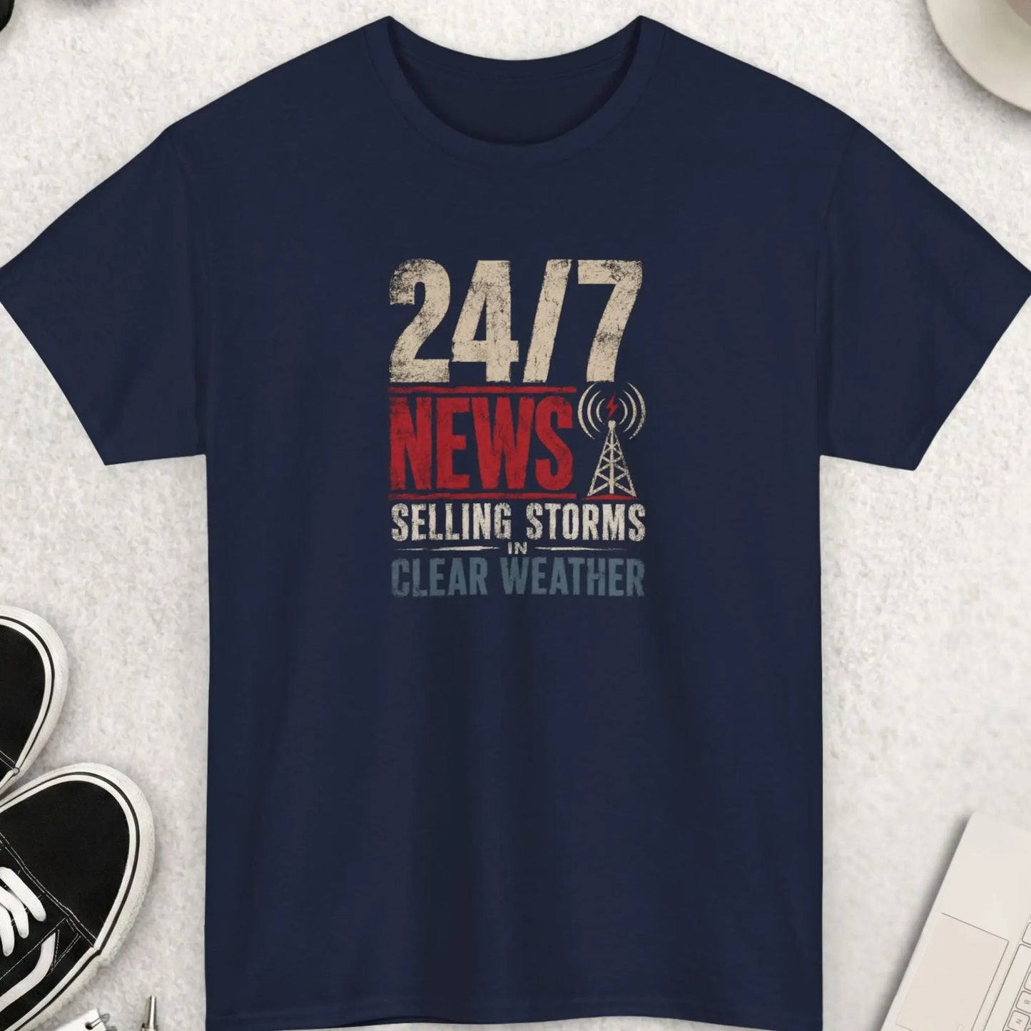 24/7 News Selling Storms In Clear Weather retro distressed typography t-shirt with broadcast antenna graphic printed on a navy blue shirt. Humorous media commentary apparel for independent thinkers, skeptics, and fans of political satire.