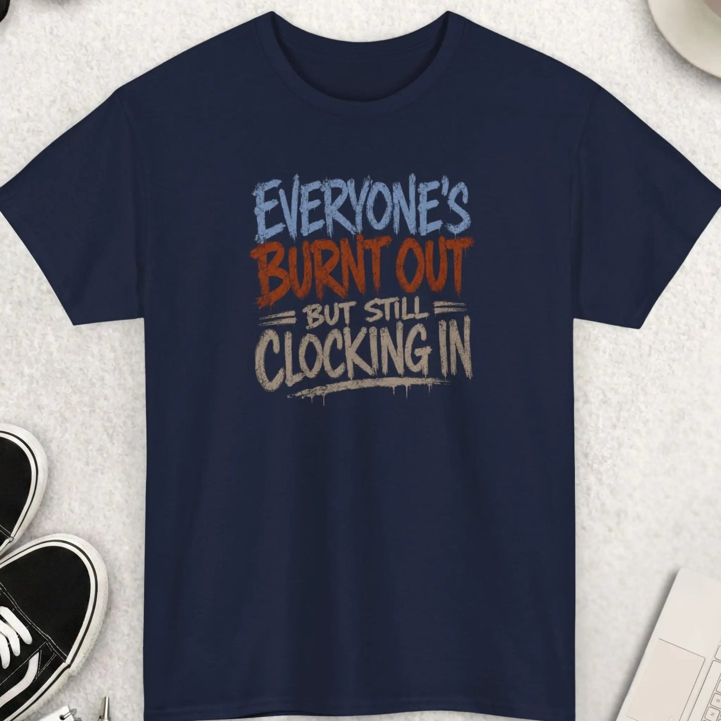 Vintage grunge graphic tee featuring the phrase “Everyone’s Burnt Out But Still Clocking In” in distressed gray and orange typography on a navy blue shirt with sarcastic burnout humor style.