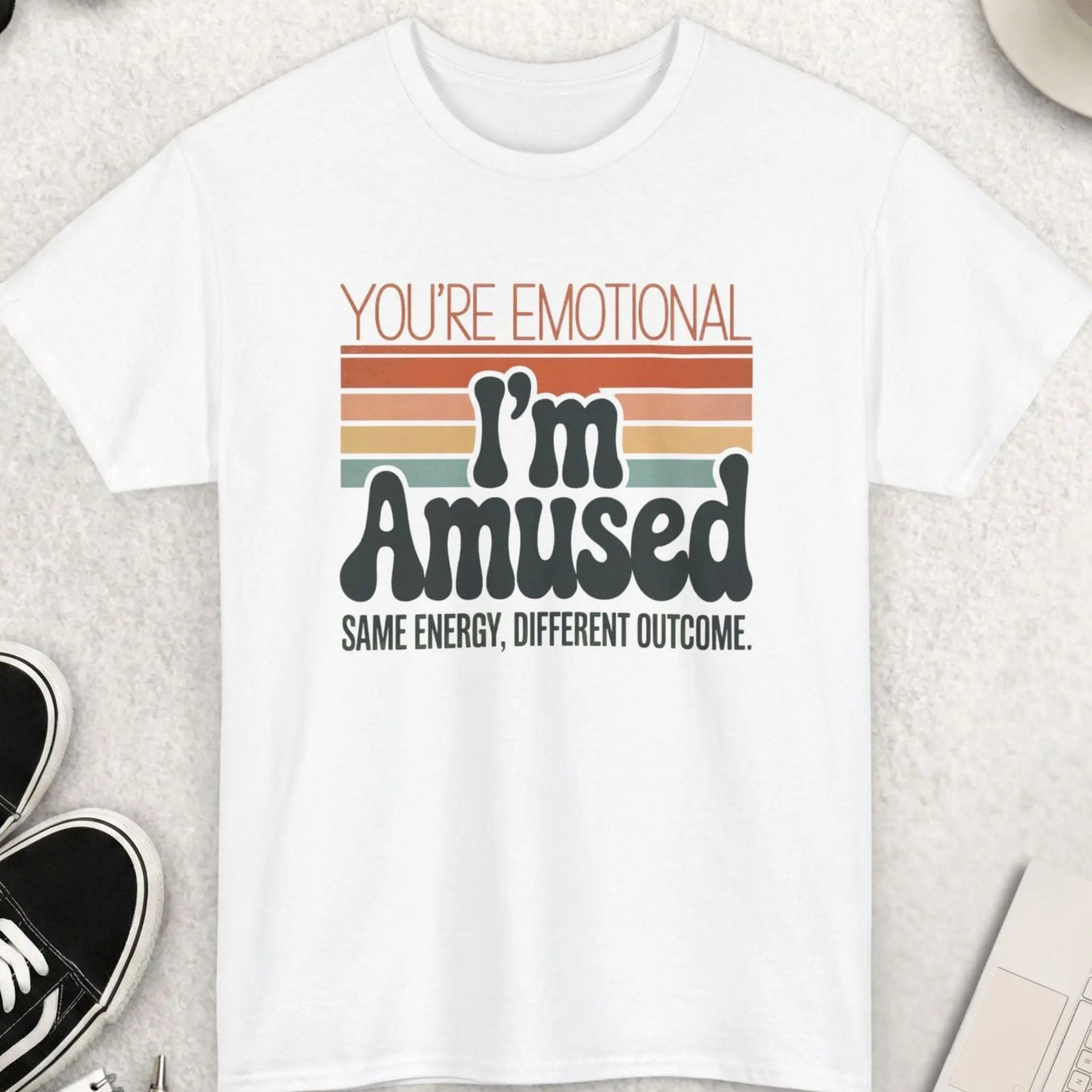 White t-shirt with humorous text design on a light gray surface with casual items.