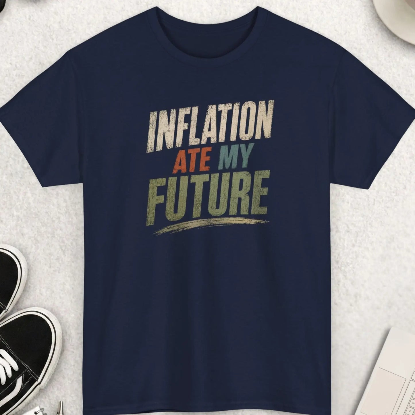 Navy blue t-shirt with distressed typography displaying the phrase “Inflation Ate My Future” in a worn vintage-style layout with muted color accents.