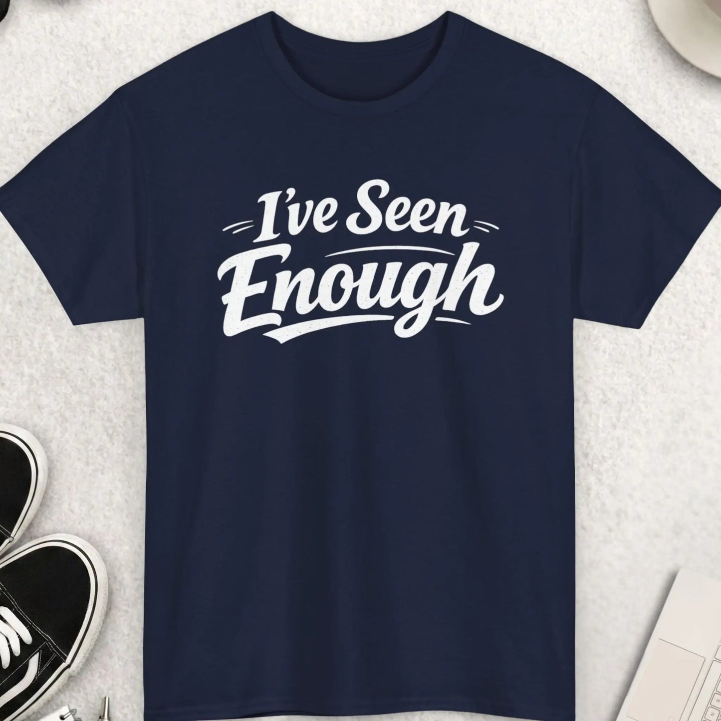 Navy blue t-shirt with 'I've Seen Enough' text on a light gray surface with accessories.