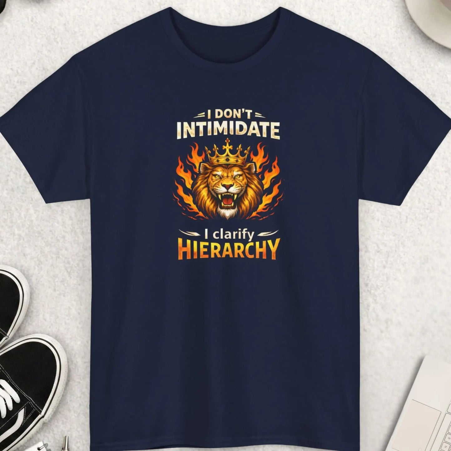 Navy blue t-shirt ' I Don’t Intimidate – I Clarify Hierarchy' on a light gray surface with accessories.