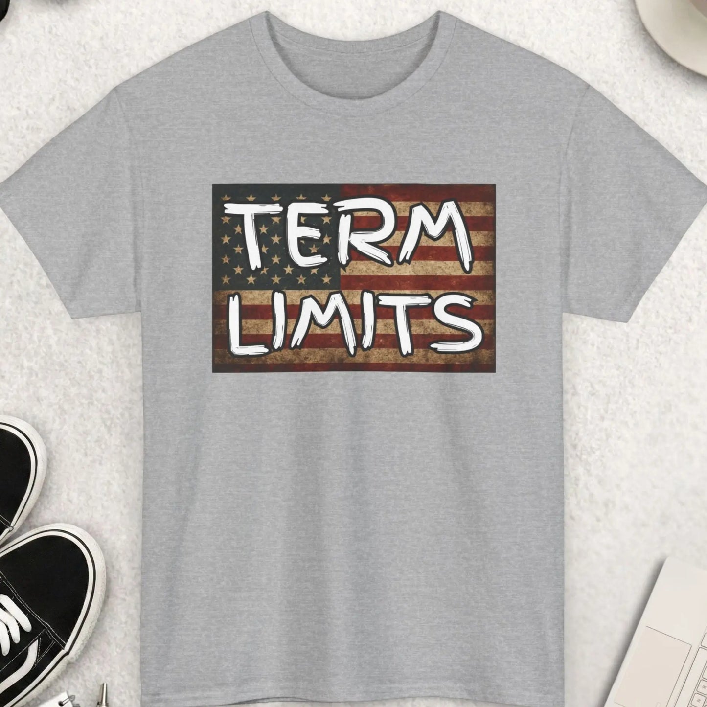 Gray t-shirt with 'TERM LIMITS' graphic on a light surface with shoes, coffee, and accessories.