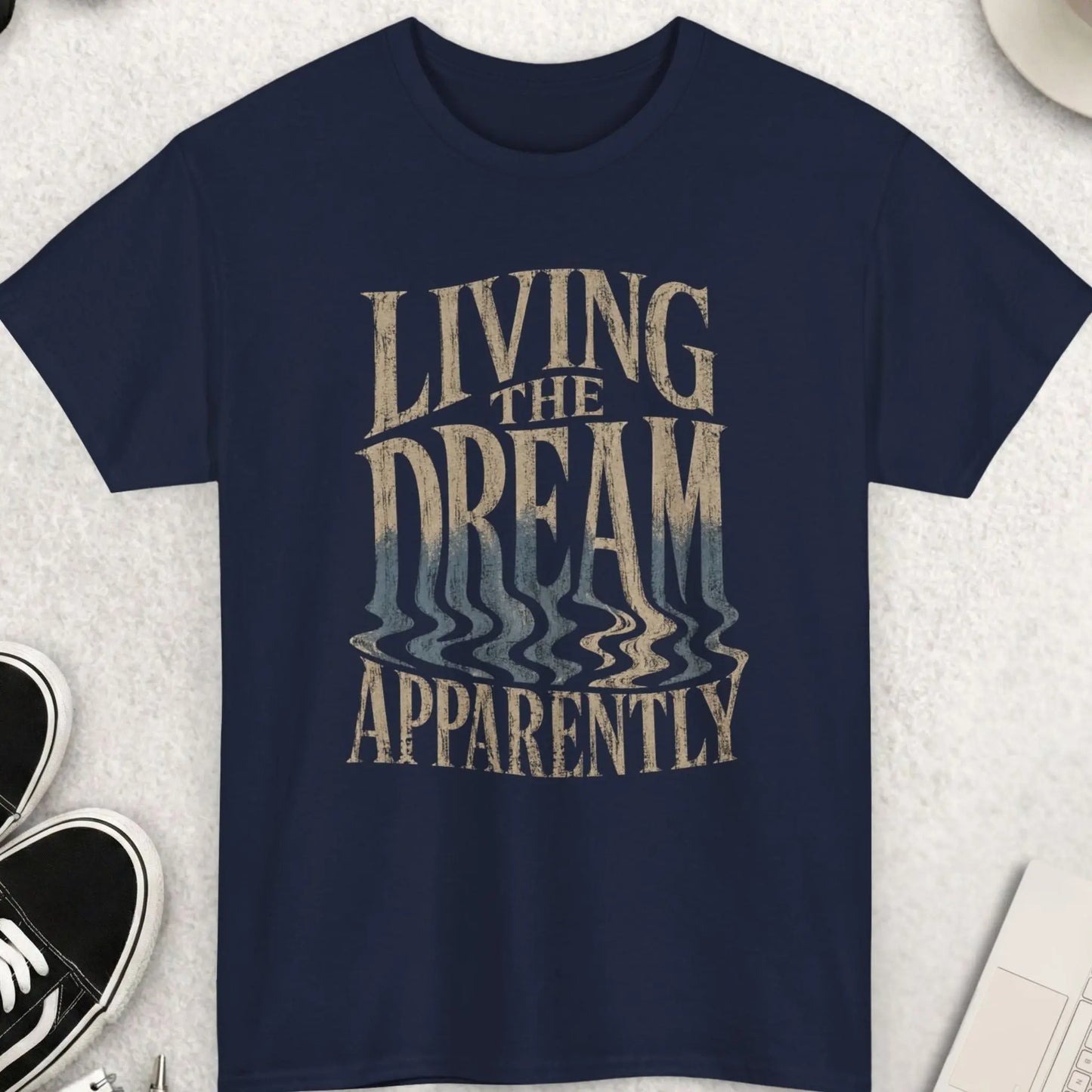Navy blue sarcastic graphic tee with distorted vintage cream and faded blue typography reading “Living The Dream Apparently” in an edgy alternative streetwear aesthetic by Mayhem Haus.
