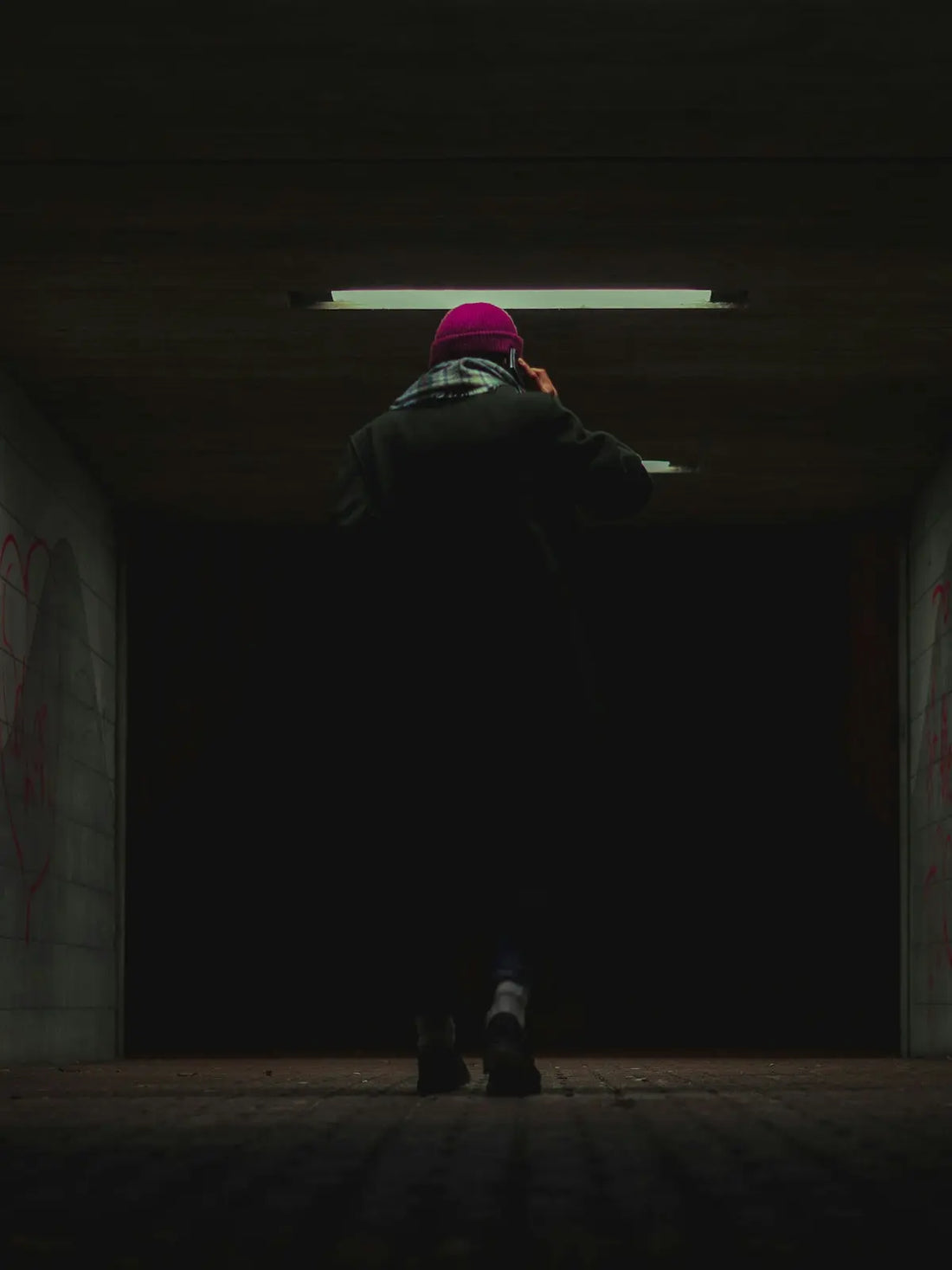 A person in a dark tunnel with a cell phone to their ear