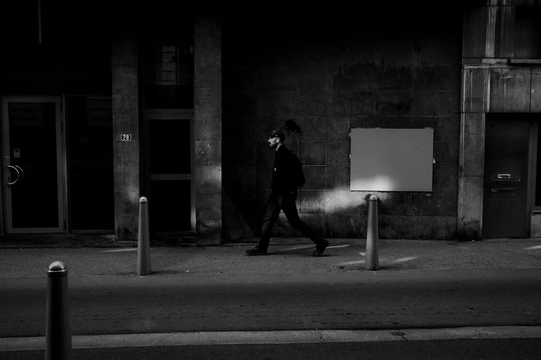 A dark figure walks past a building.