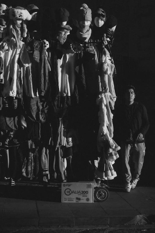 A person stands near a clothing rack at night.
