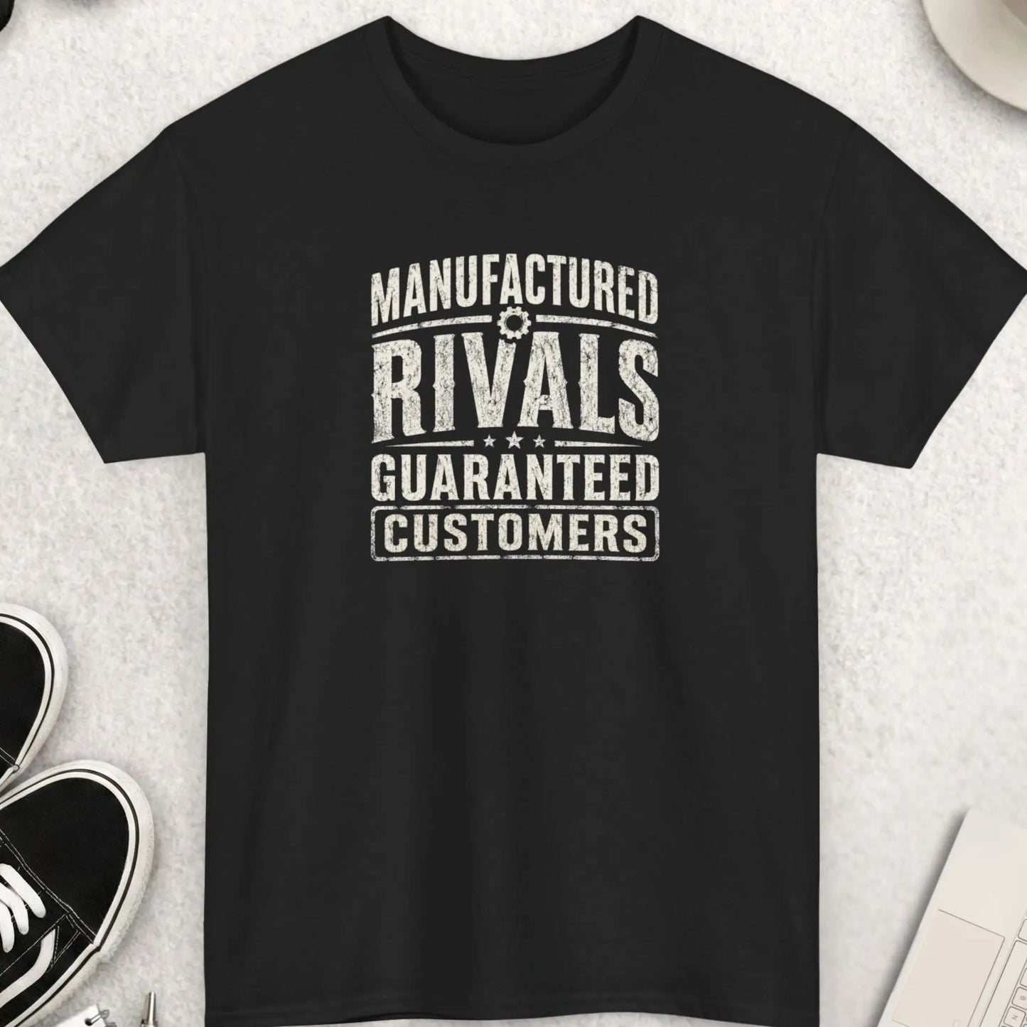 Manufactured Rivals Guaranteed Customers distressed typography t-shirt featuring large vintage cream lettering on a black shirt with weathered texture, industrial-inspired design, and bold statement message.