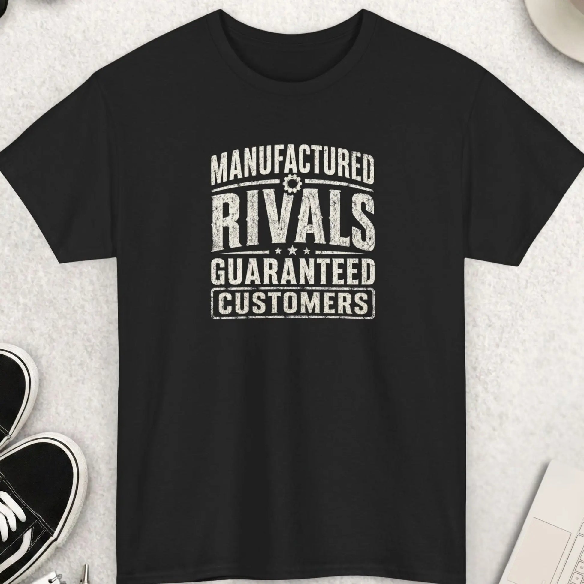 Manufactured Rivals Guaranteed Customers distressed typography t-shirt featuring large vintage cream lettering on a black shirt with weathered texture, industrial-inspired design, and bold statement message.