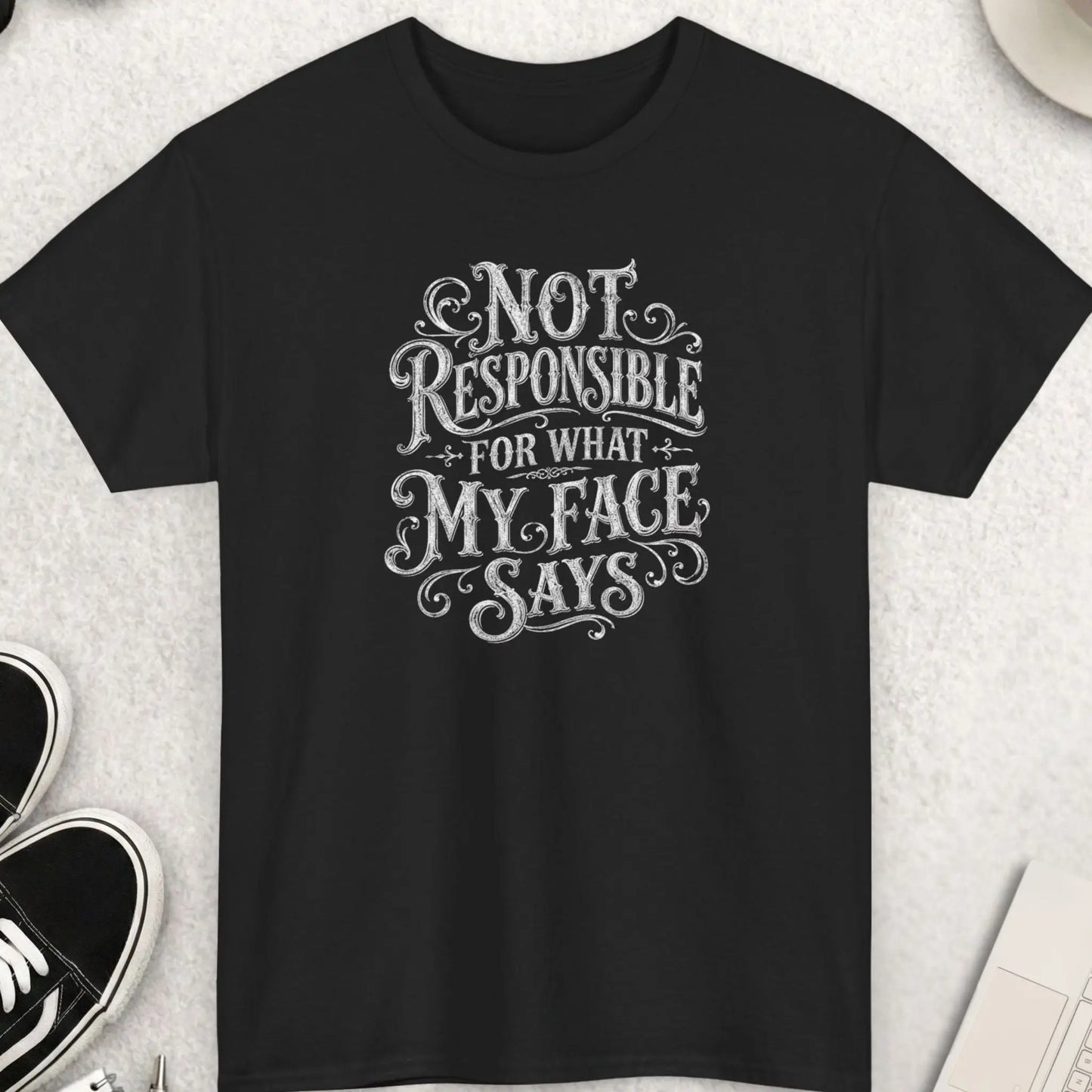 Black vintage typography graphic t-shirt featuring the phrase “Not Responsible For What My Face Says” in distressed white ornate lettering with decorative flourishes and retro styling.