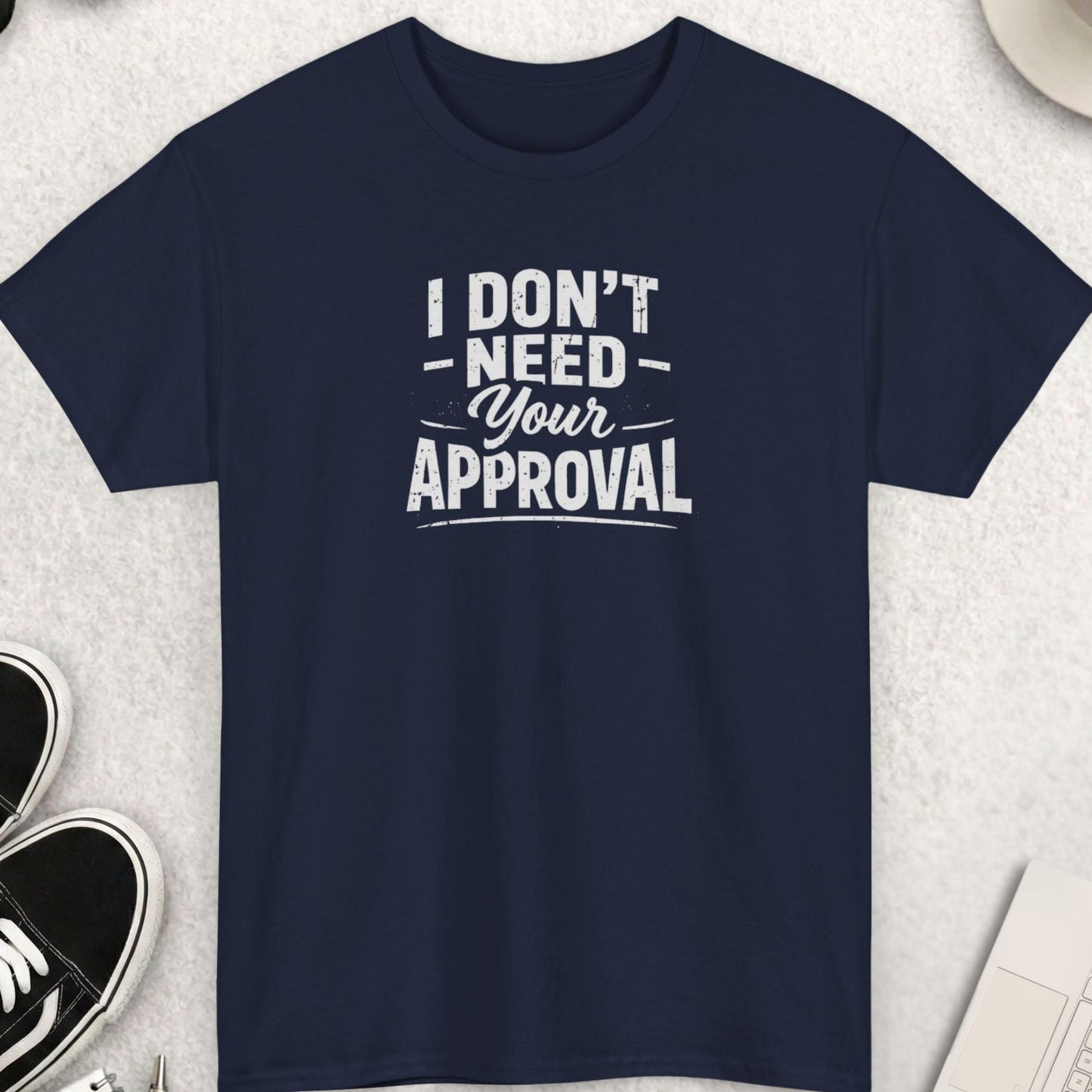 Navy blue t-shirt with 'I don't need your approval' text on a light gray surface with shoes, coffee, and accessories.