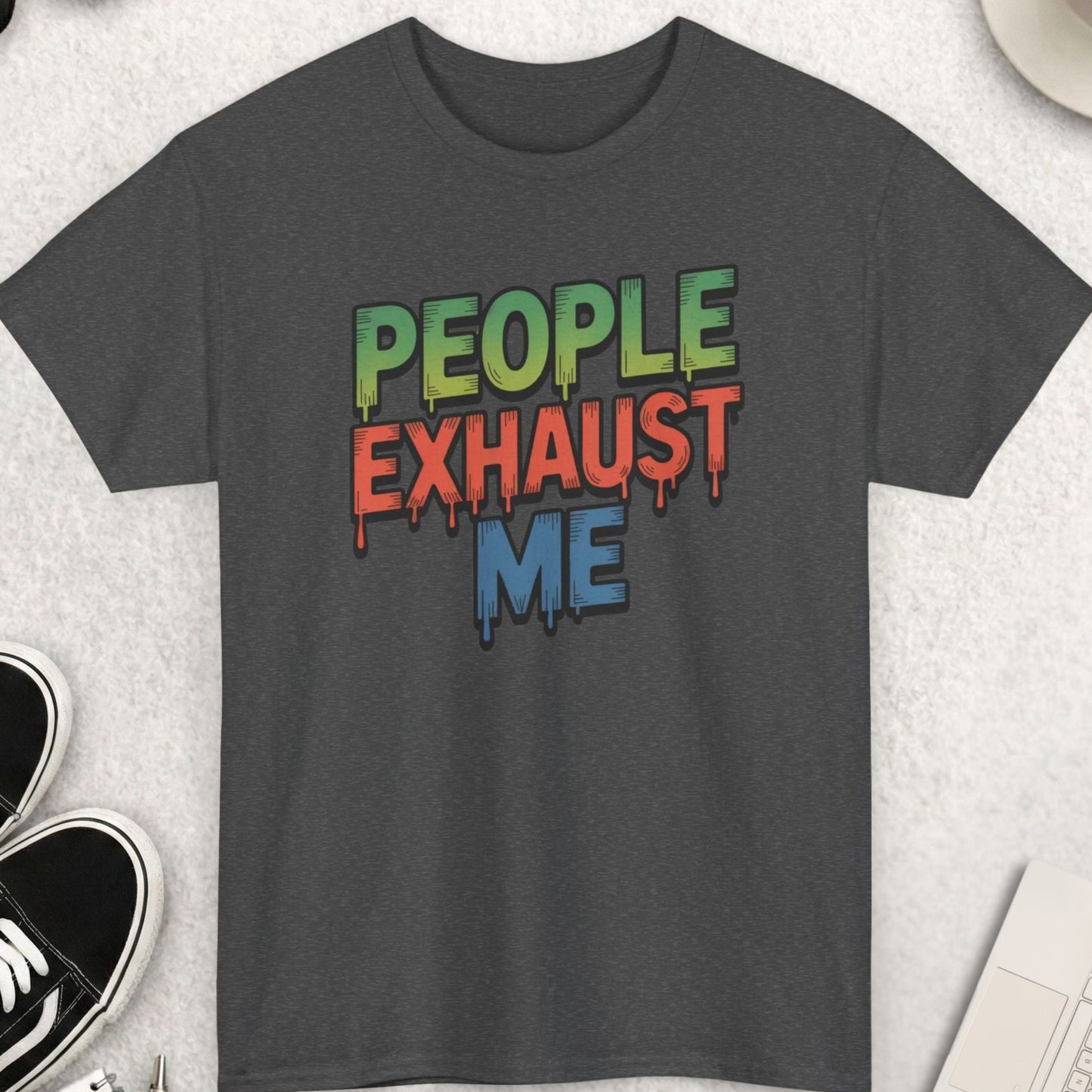 Gray t-shirt with colorful text 'PEOPLE EXHAUST ME' on a light gray surface with accessories.
