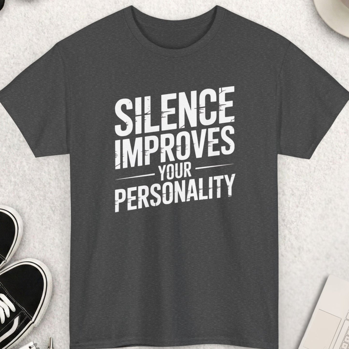 Gray t-shirt with 'Silence Improves Your Personality' text on a light gray surface with shoes, coffee, and sunglasses.