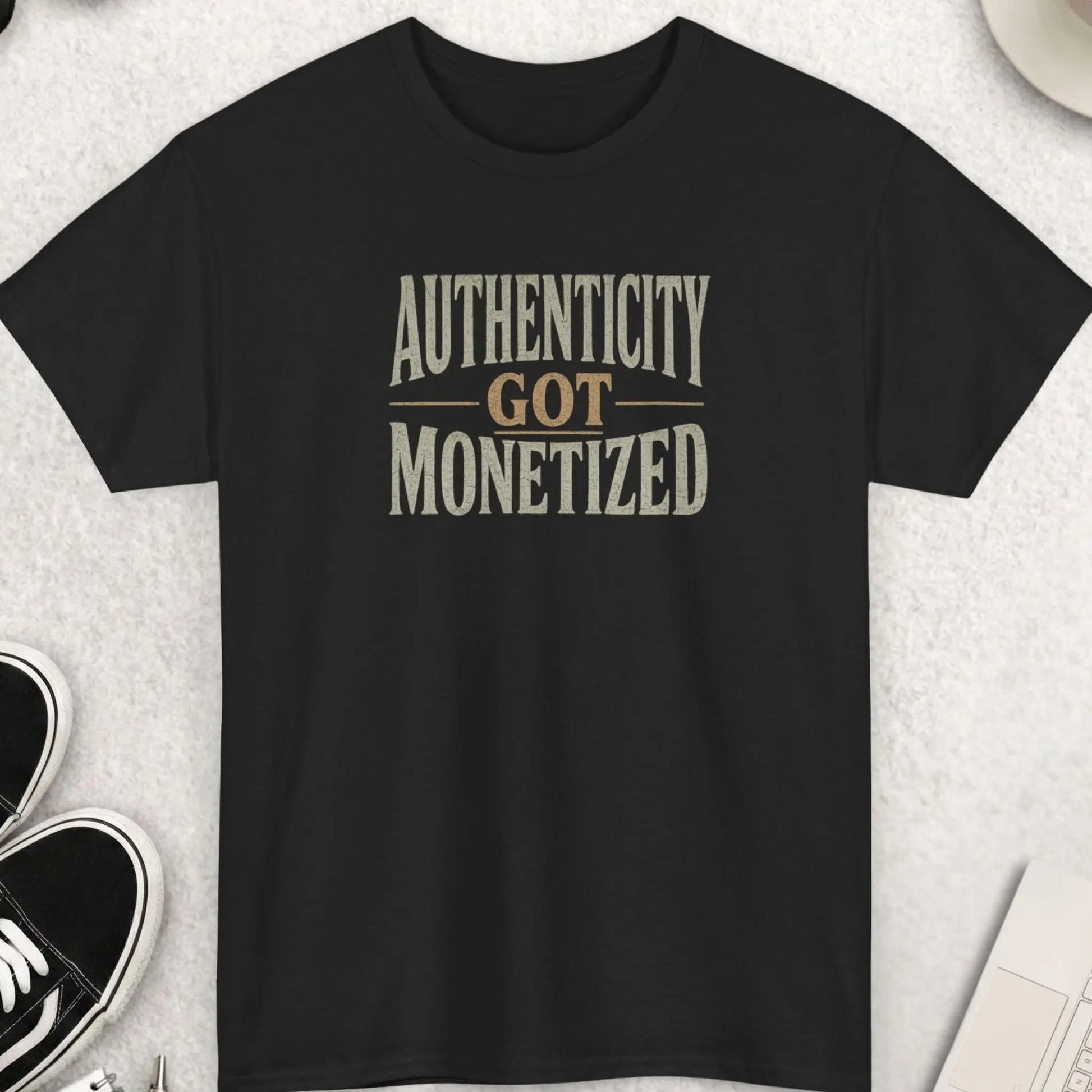 Black graphic t-shirt featuring distressed vintage typography reading “Authenticity Got Monetized” in muted earth-tone lettering.