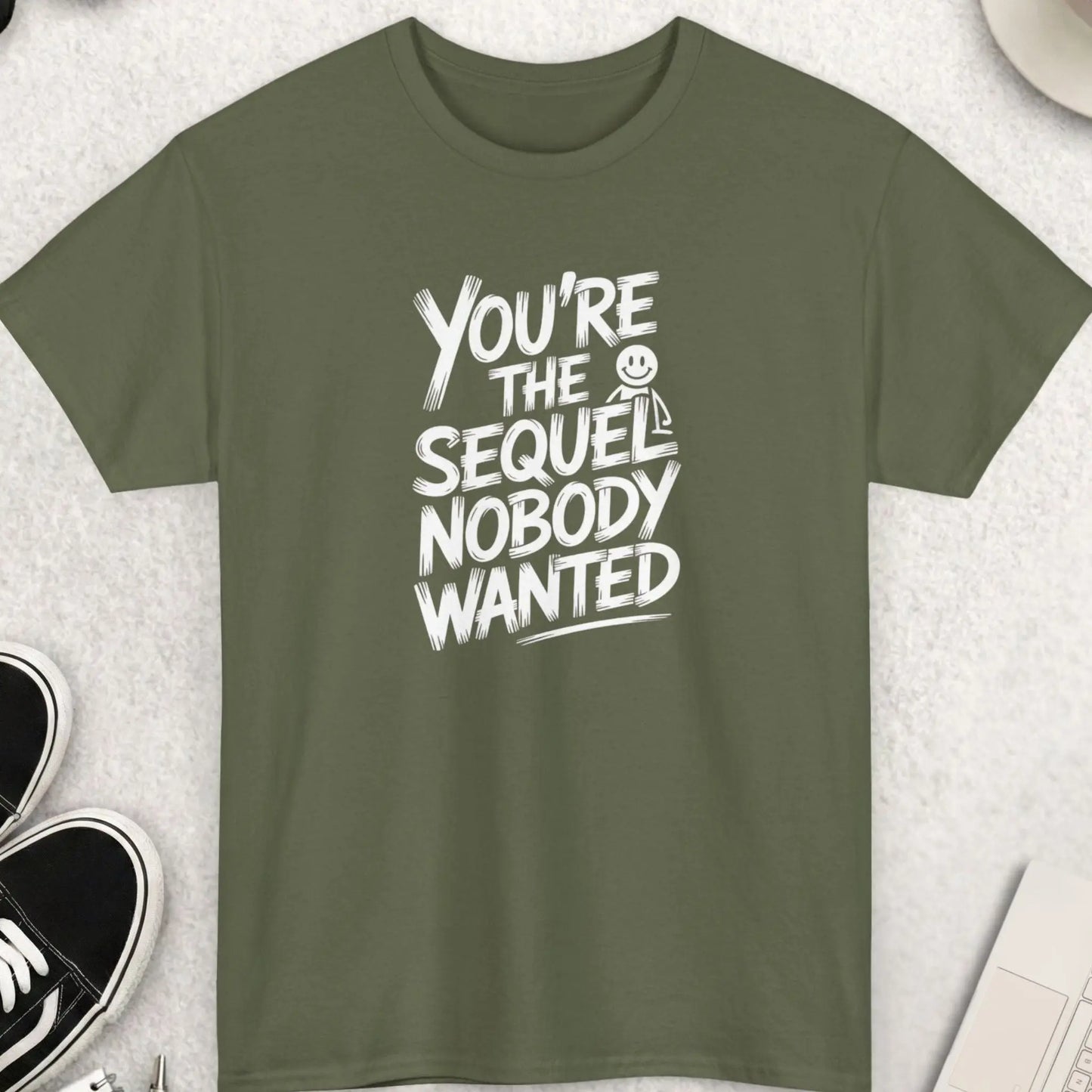 military green t-shirt with white text on a light gray surface with accessories.