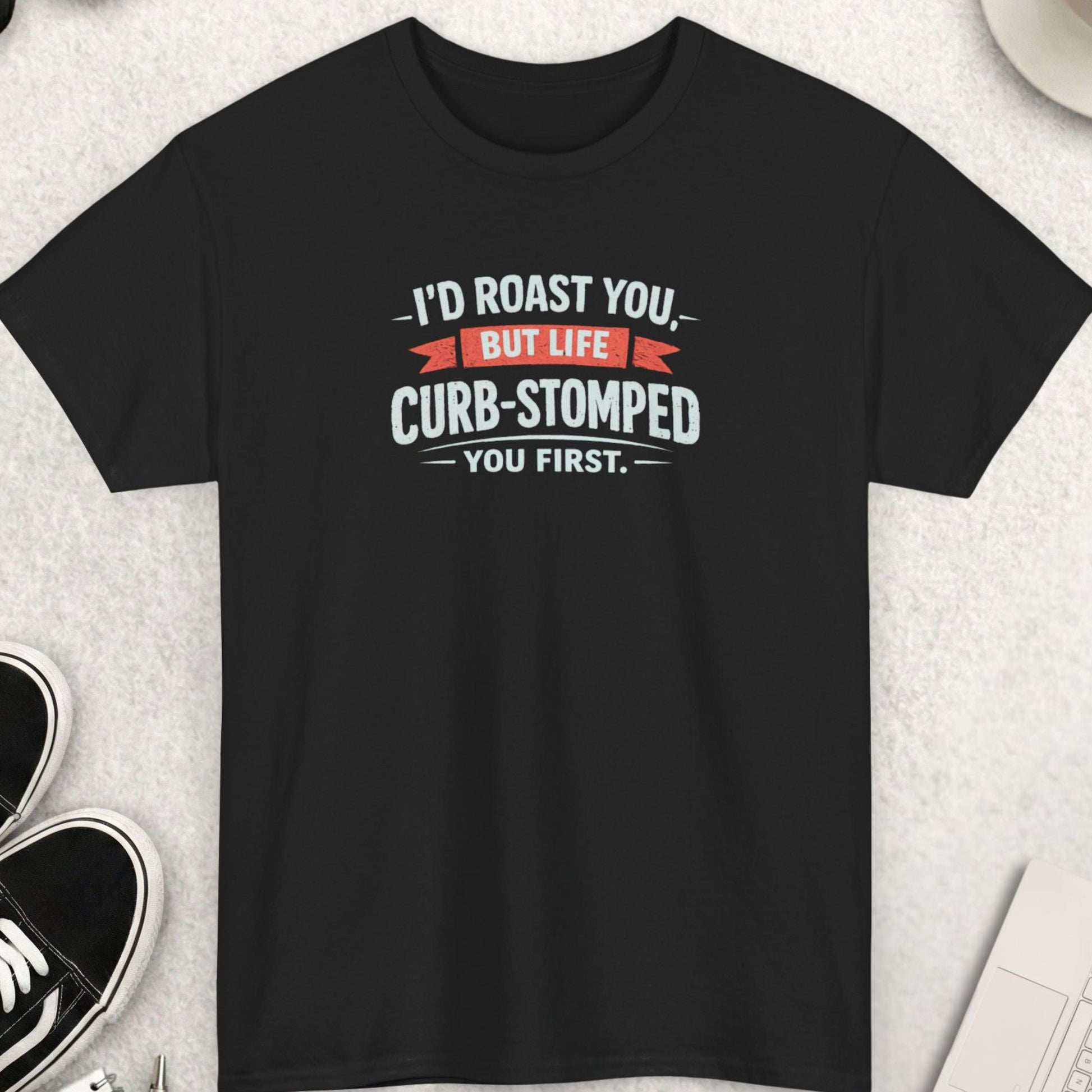Black t-shirt with humorous text on a light gray surface with shoes, coffee, and sunglasses.
