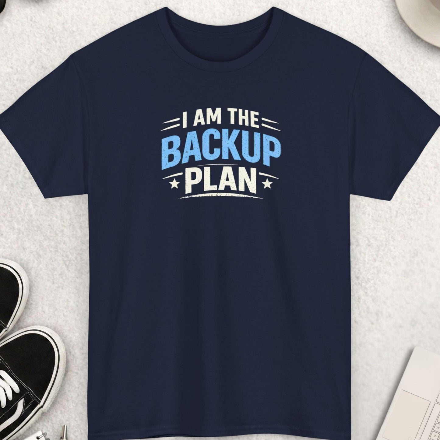 Navy blue t-shirt with 'I am the backup plan' text on a light gray surface with accessories.