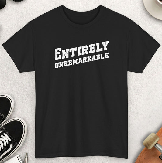 Black t-shirt with 'ENTIRELY UNREMARKABLE' text on a light gray surface with accessories.