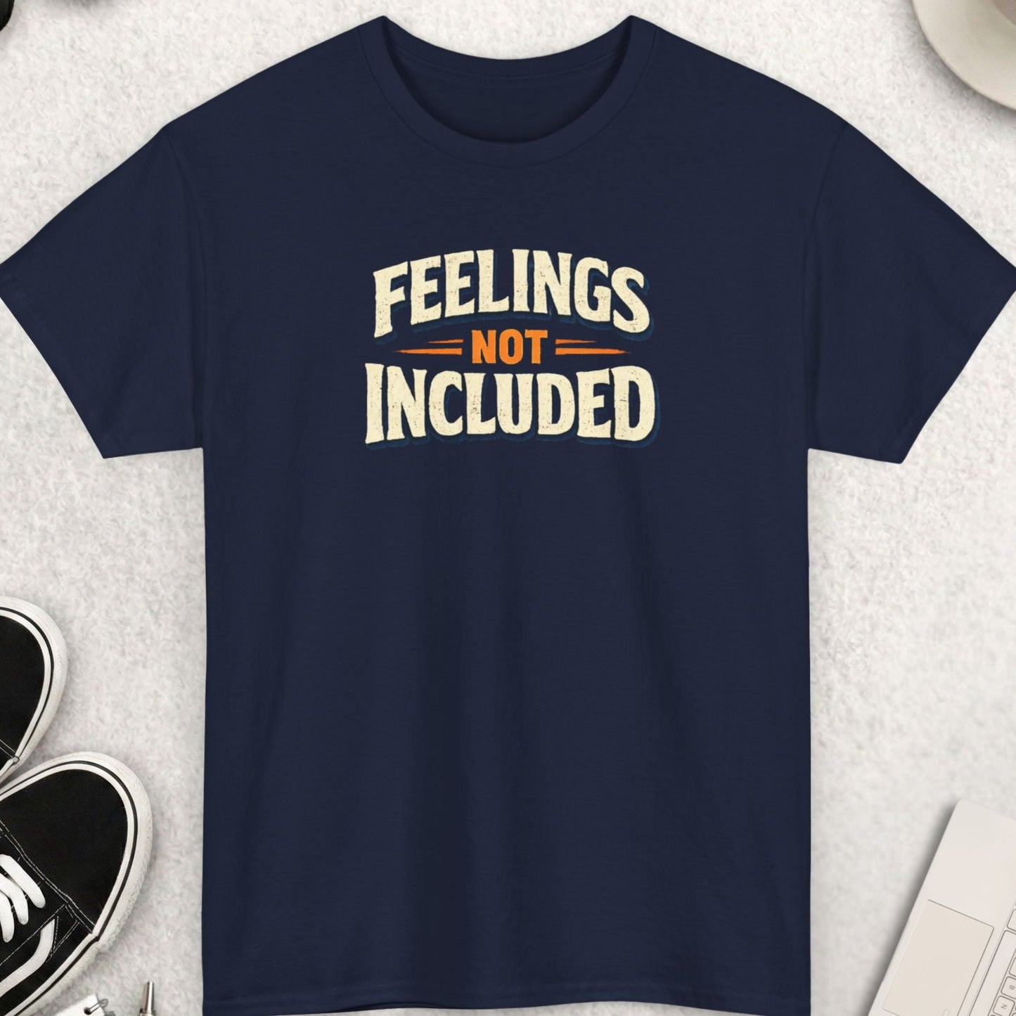 Navy blue t-shirt with 'Feelings Not Included' text on a light gray surface with accessories.