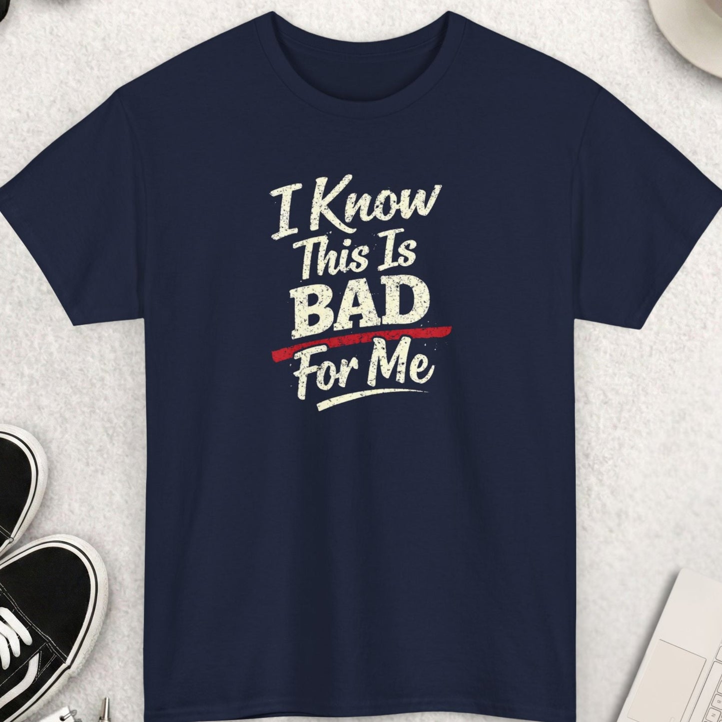Navy blue t-shirt with humorous text design on a light gray surface with accessories.