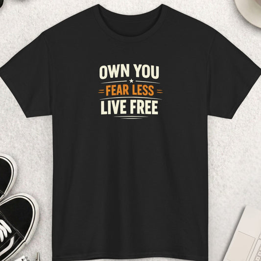 Black t-shirt with 'OWN YOU. FEAR LESS. LIVE FREE' text on a light gray surface with shoes, sunglasses, and a cup.