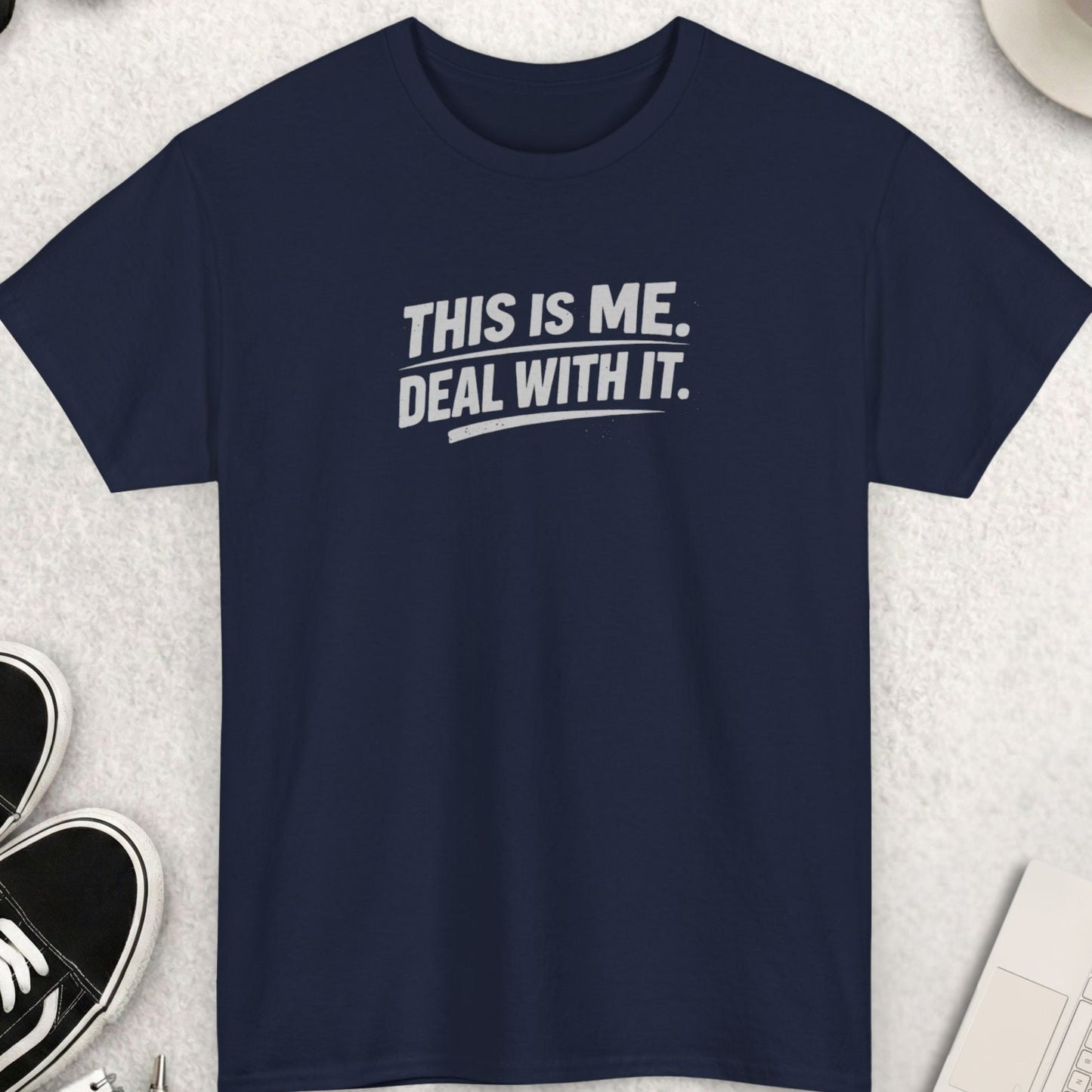 Navy blue t-shirt with 'THIS IS ME. DEAL WITH IT.' text on a light gray surface with shoes, coffee, and accessories.
