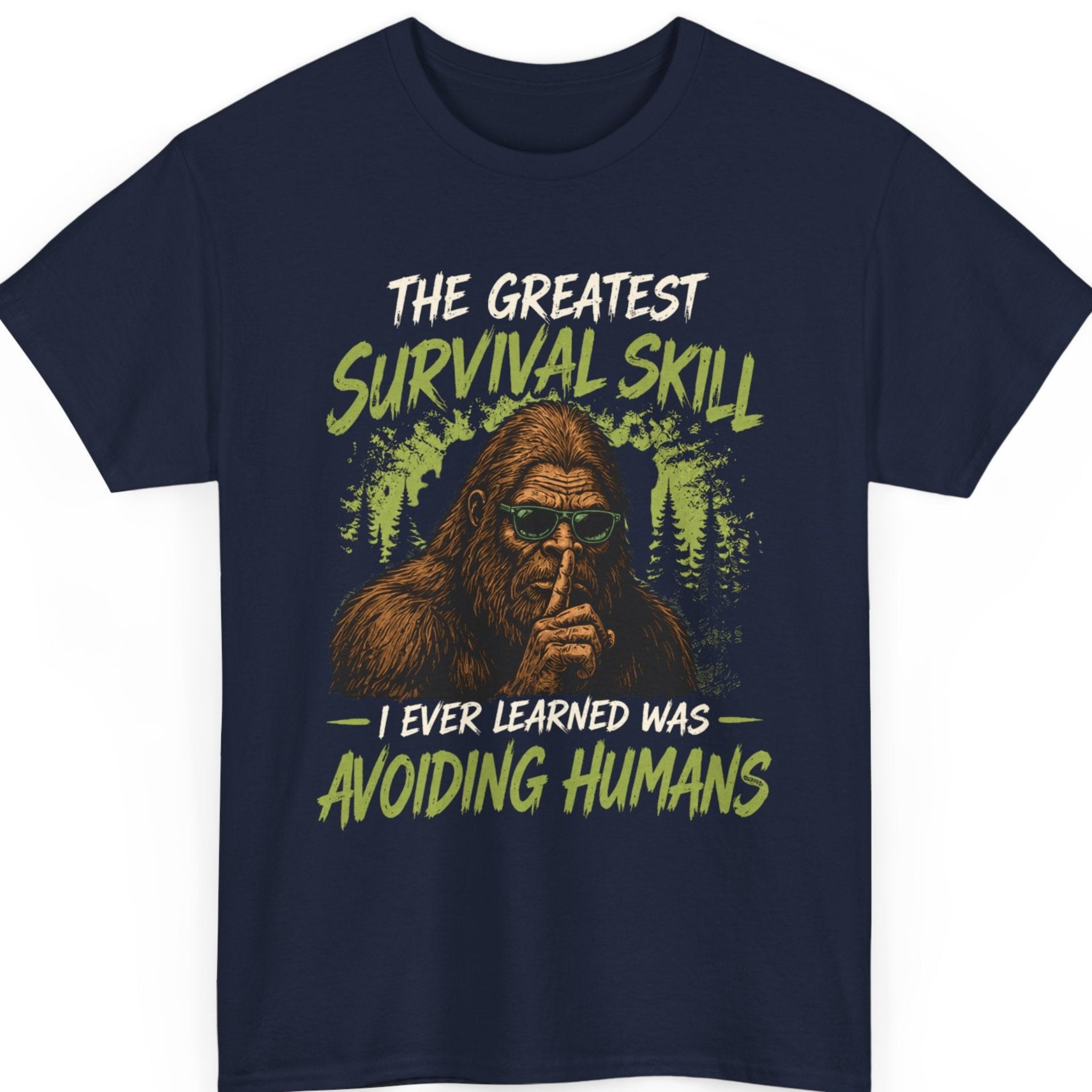 Mayhem Haus Sasquatch t-shirt on a navy blue shirt featuring a realistic Bigfoot illustration with sunglasses, woodland scenery, distressed typography, and the humorous phrase "The Greatest Survival Skill I Ever Learned Was Avoiding Humans."