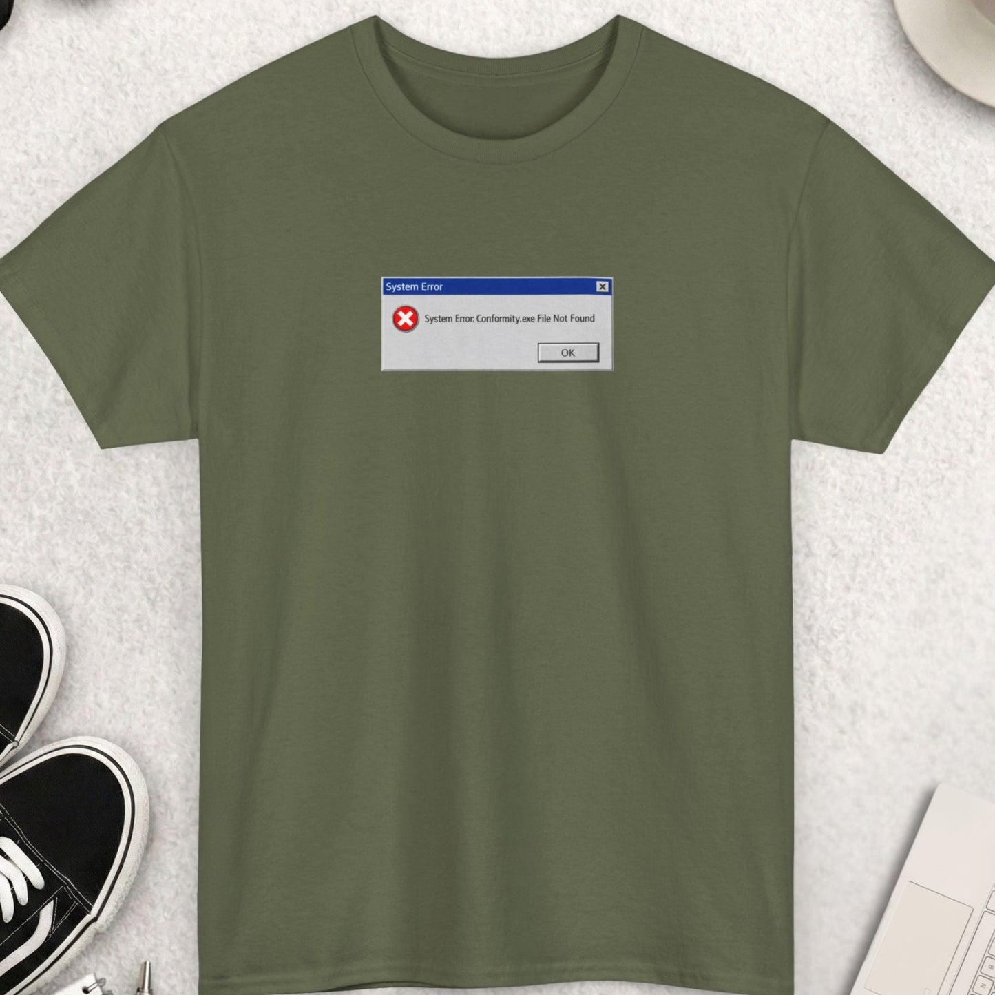 Green t-shirt with a graphic on a light gray surface with shoes, sunglasses, and a cup of coffee.