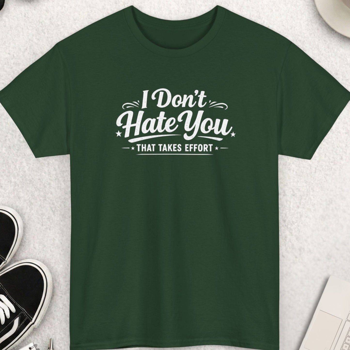 Green t-shirt with 'I Don't Hate You That Takes Effort' text on a light gray surface with shoes, sunglasses, and coffee.