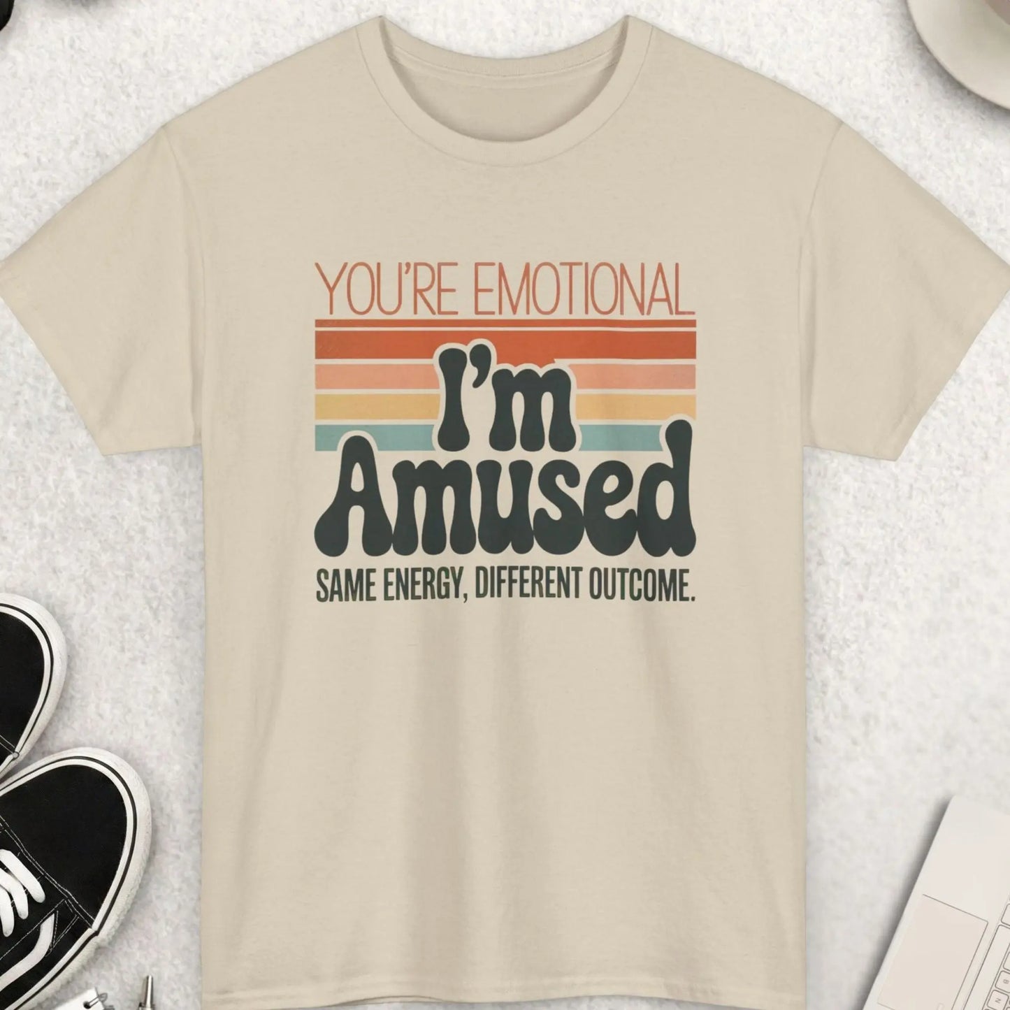 Beige t-shirt with humorous text design on a light gray surface with accessories.