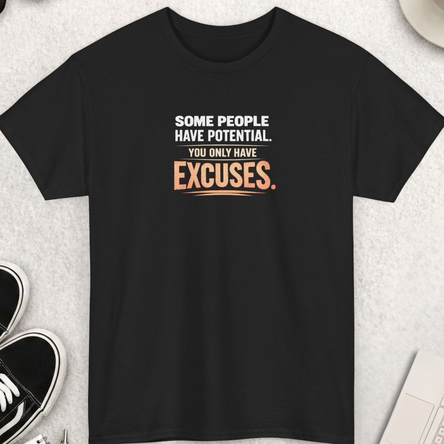 Black t-shirt with motivational quote on a light gray surface with shoes, coffee, and accessories.