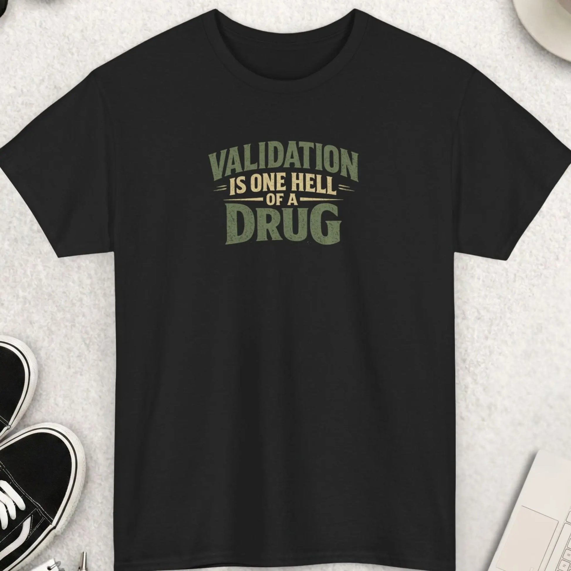 Black t-shirt featuring distressed vintage typography reading “Validation Is One Hell Of A Drug” in muted earth-tone colors with a bold minimalist layout.