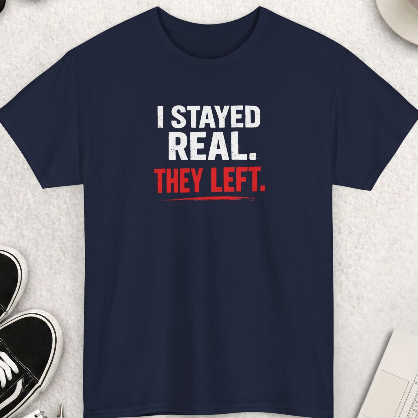 Navy blue t-shirt with humorous text on a light gray surface with accessories.