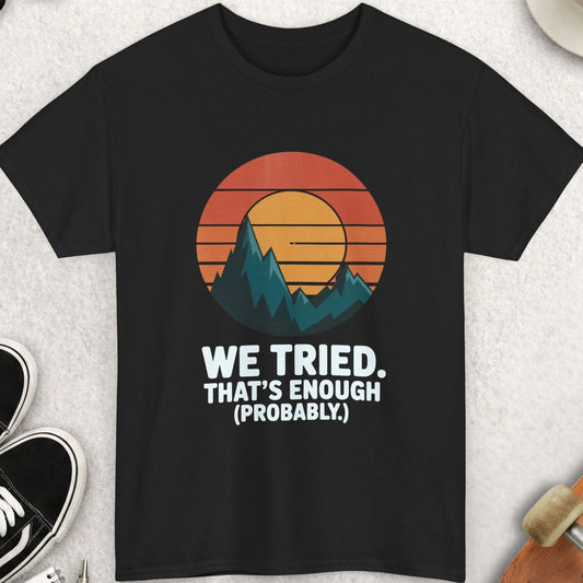 Black t-shirt with mountain graphic and text on a light gray surface with accessories.