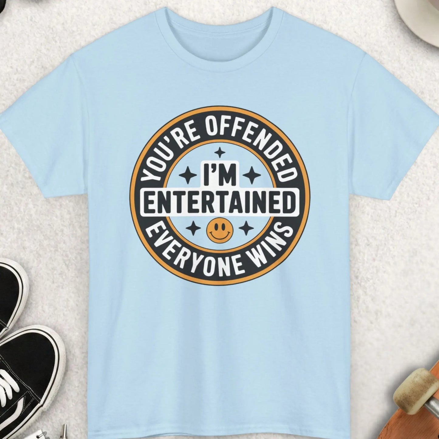 Light blue t-shirt with a humorous graphic design on a textured surface with accessories.