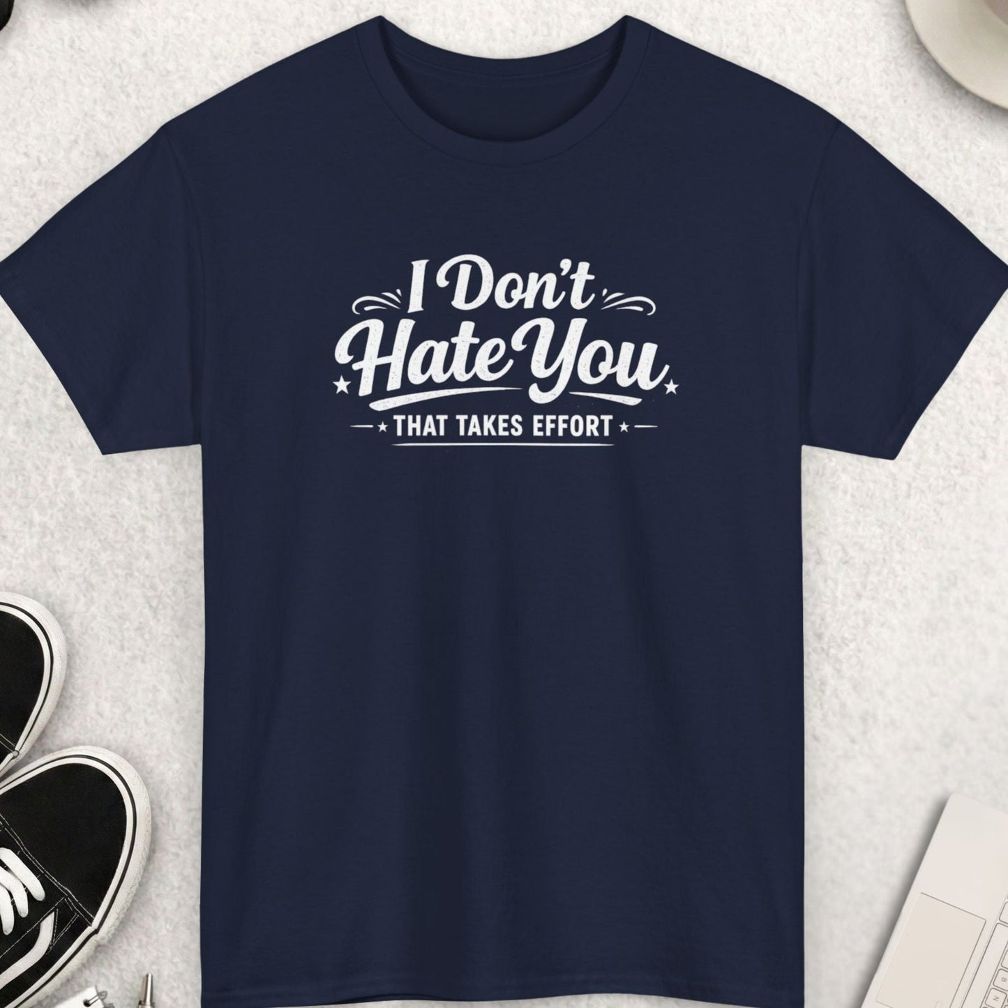 Navy blue t-shirt with 'I Don't Hate You That Takes Effort' text on a light gray surface with accessories.