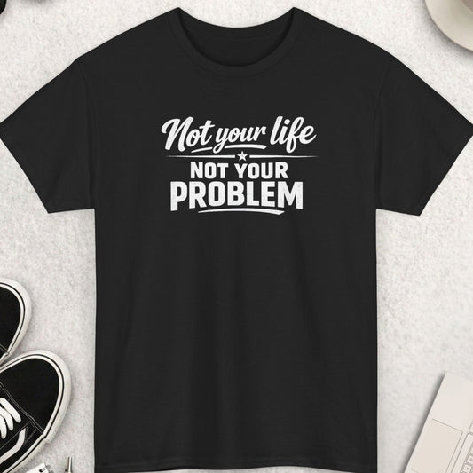 Black t-shirt with 'Not your life, not your problem' text on a light gray surface with shoes, coffee, and accessories.